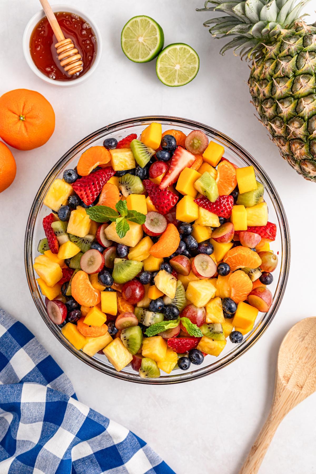 A bowl of mixed fruit salad with strawberries, mango, blueberries, kiwi, and grapes on a white table.