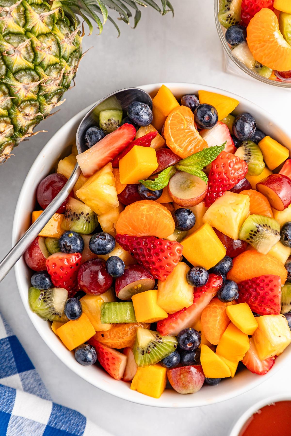 A bowl of colorful mixed fruit salad with strawberries, blueberries, pineapple, kiwi, grapes, and mango.