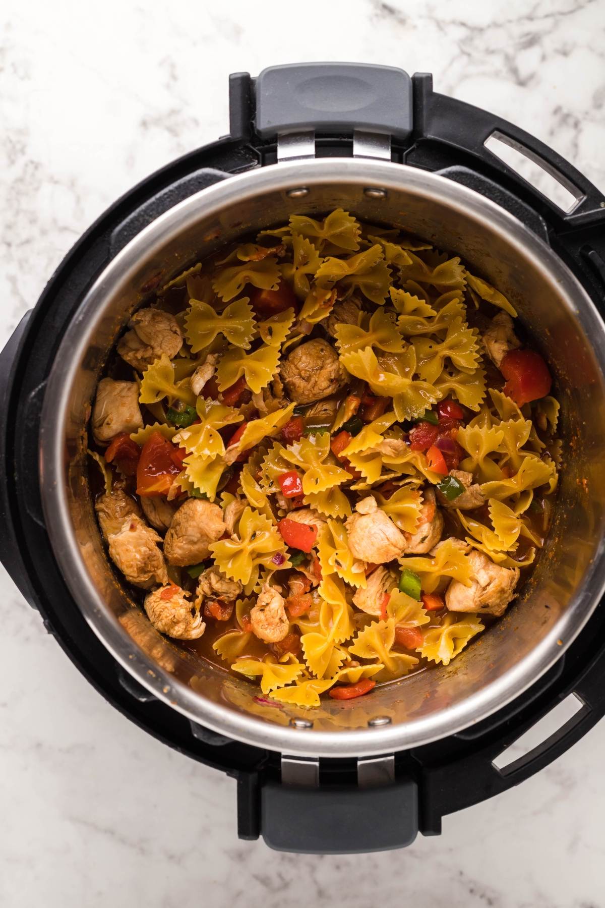 Bowtie pasta, chicken, and vegetables come together for an easy instant pot chicken pasta dinner, all cooked in one pot and captured from above on a marble surface.