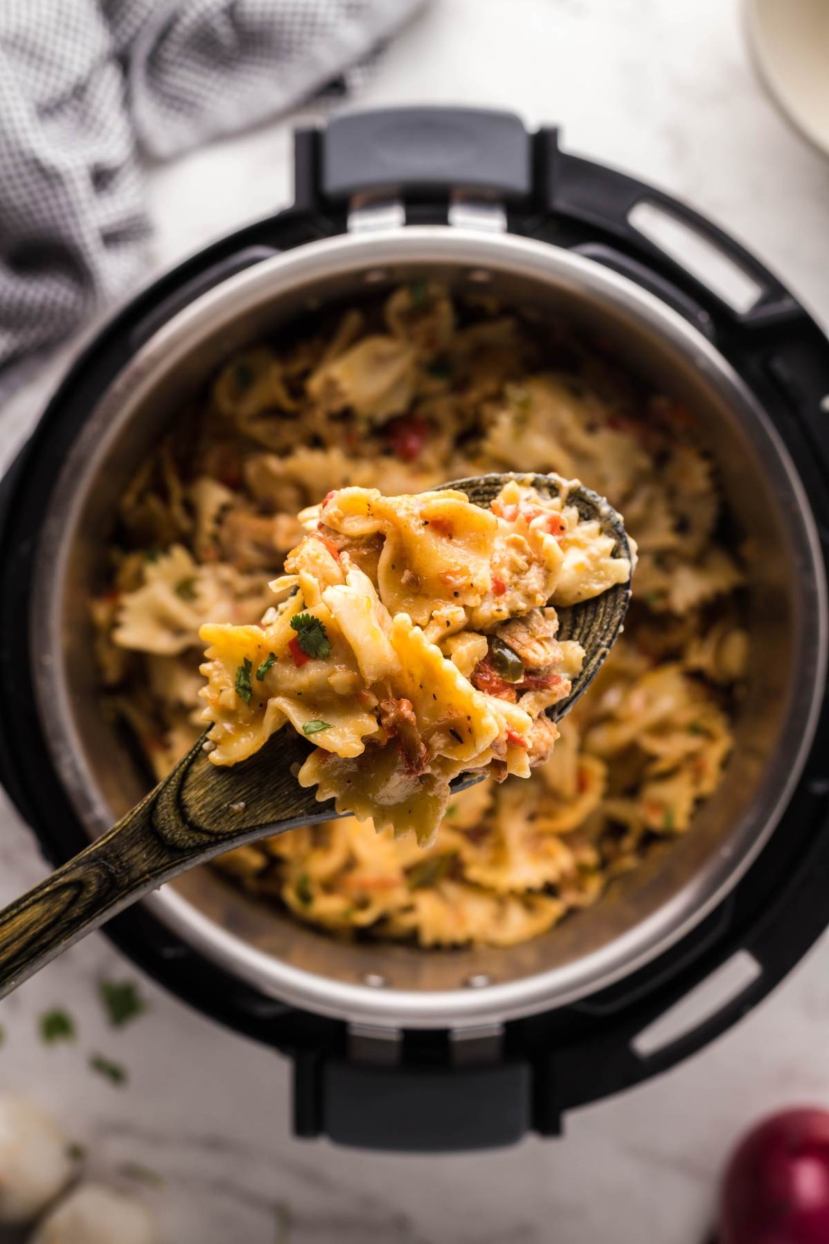 A wooden spoon holds bowtie pasta with vegetables and sauce above an Instant Pot filled with a flavorful pasta dinner in an instant pot.