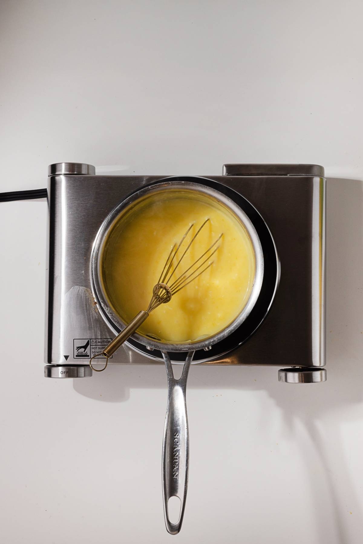A saucepan with yellow sauce and a whisk on an electric stovetop, viewed from above.