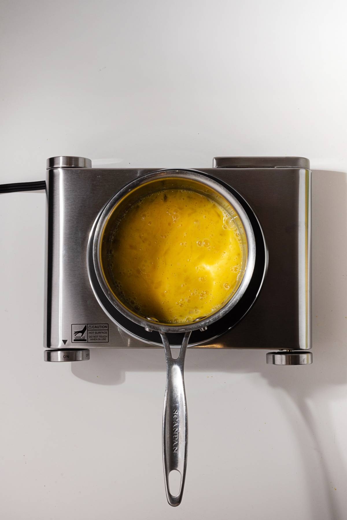 A metal saucepan with beaten eggs sits on an electric stovetop, ready to be cooked.