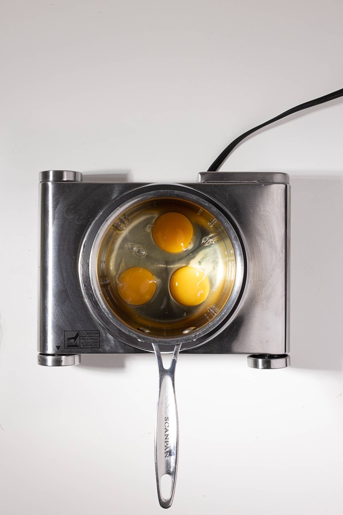Three raw eggs in a saucepan on an electric cooktop, viewed from above.