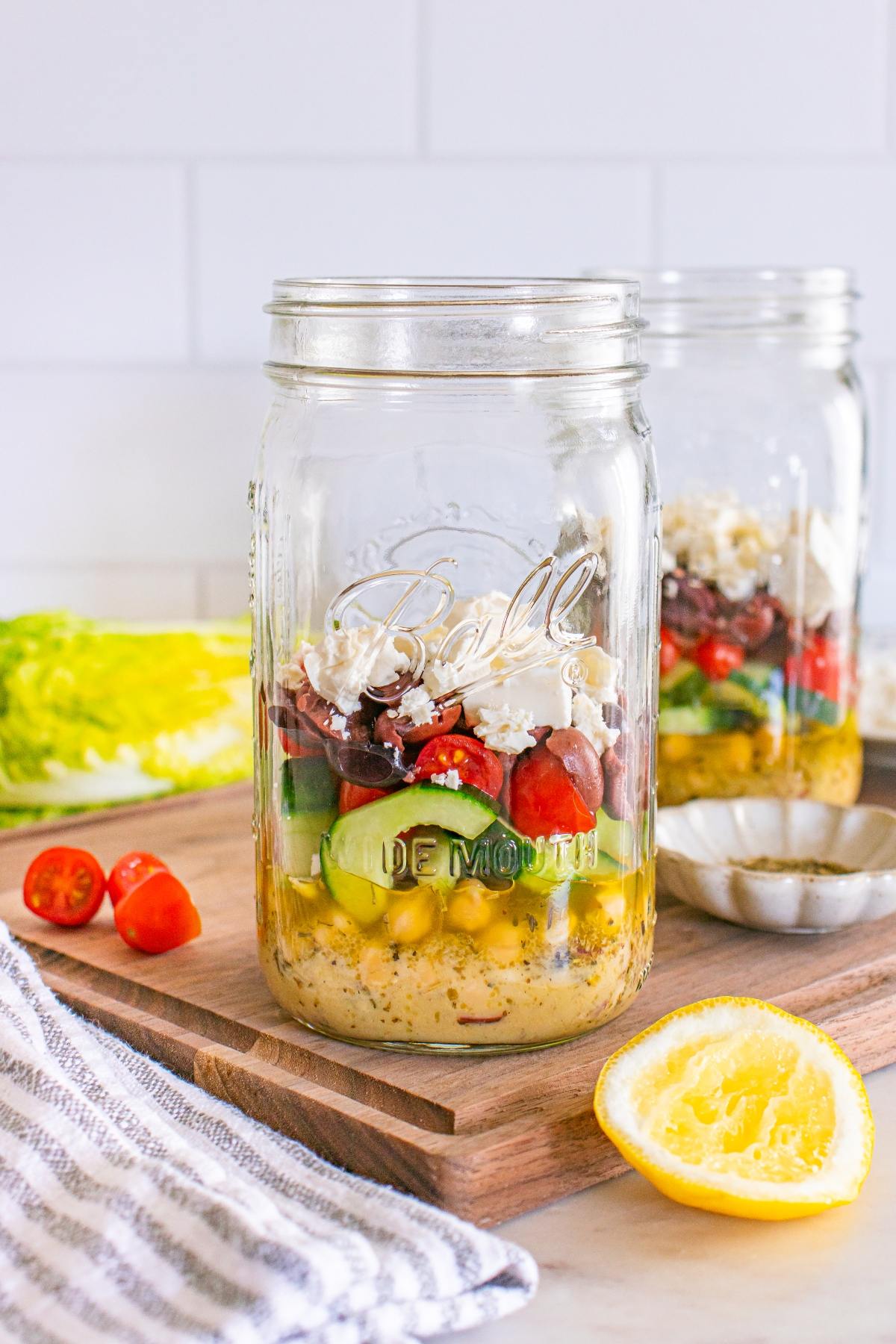 A mason jar layered with salad ingredients like chickpeas, cucumbers, tomatoes, olives, and feta cheese.