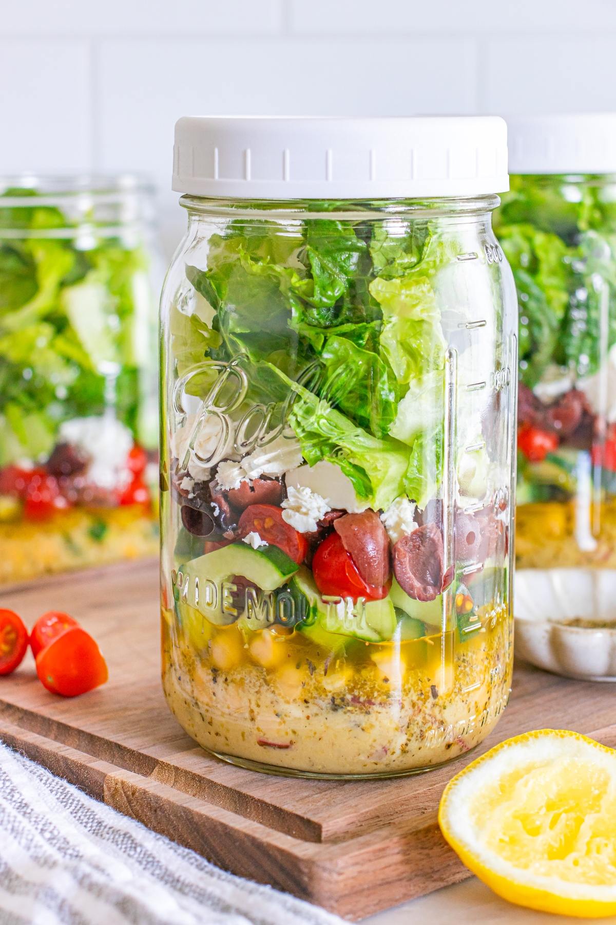 A mason jar layered with salad ingredients, including lettuce, tomatoes, olives, and chickpeas.