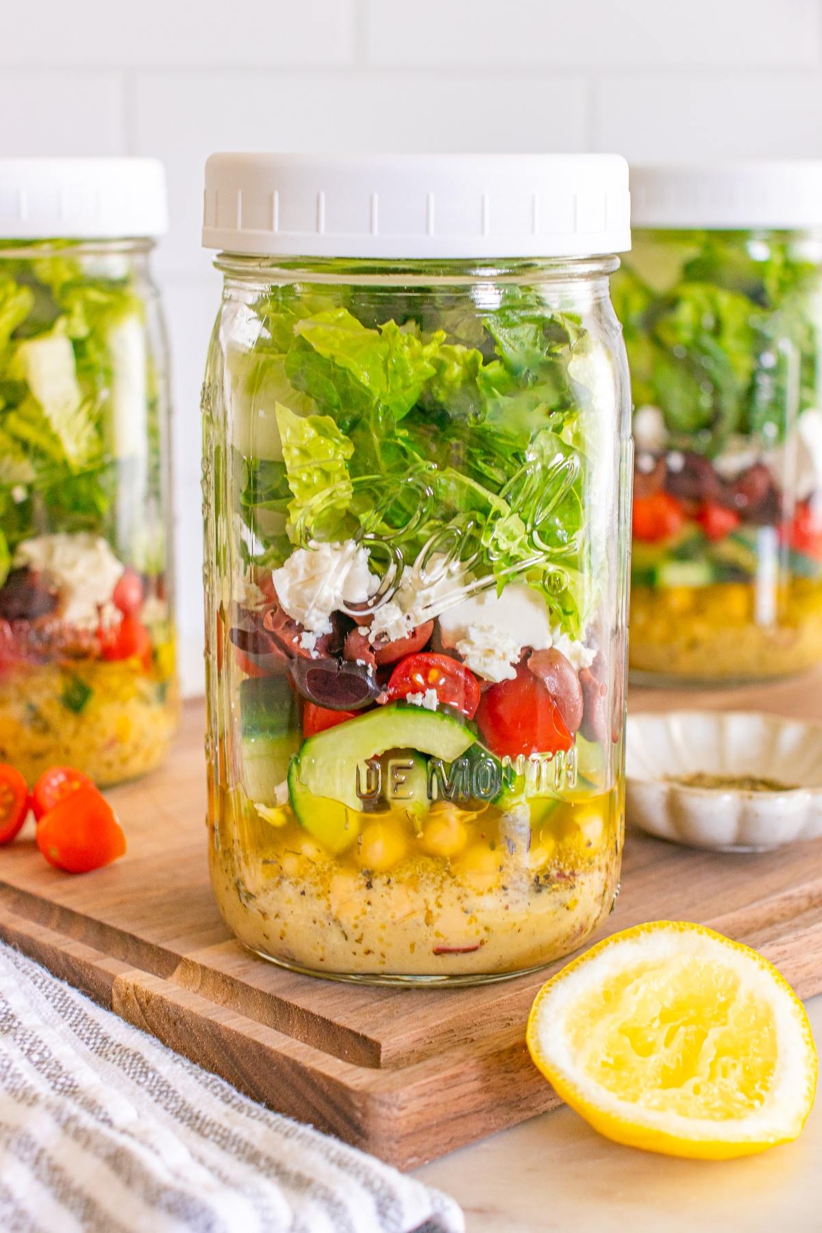 Greek salad in a mason jar with layers of dressing, corn, cucumbers, tomatoes, olives, feta, and lettuce.
