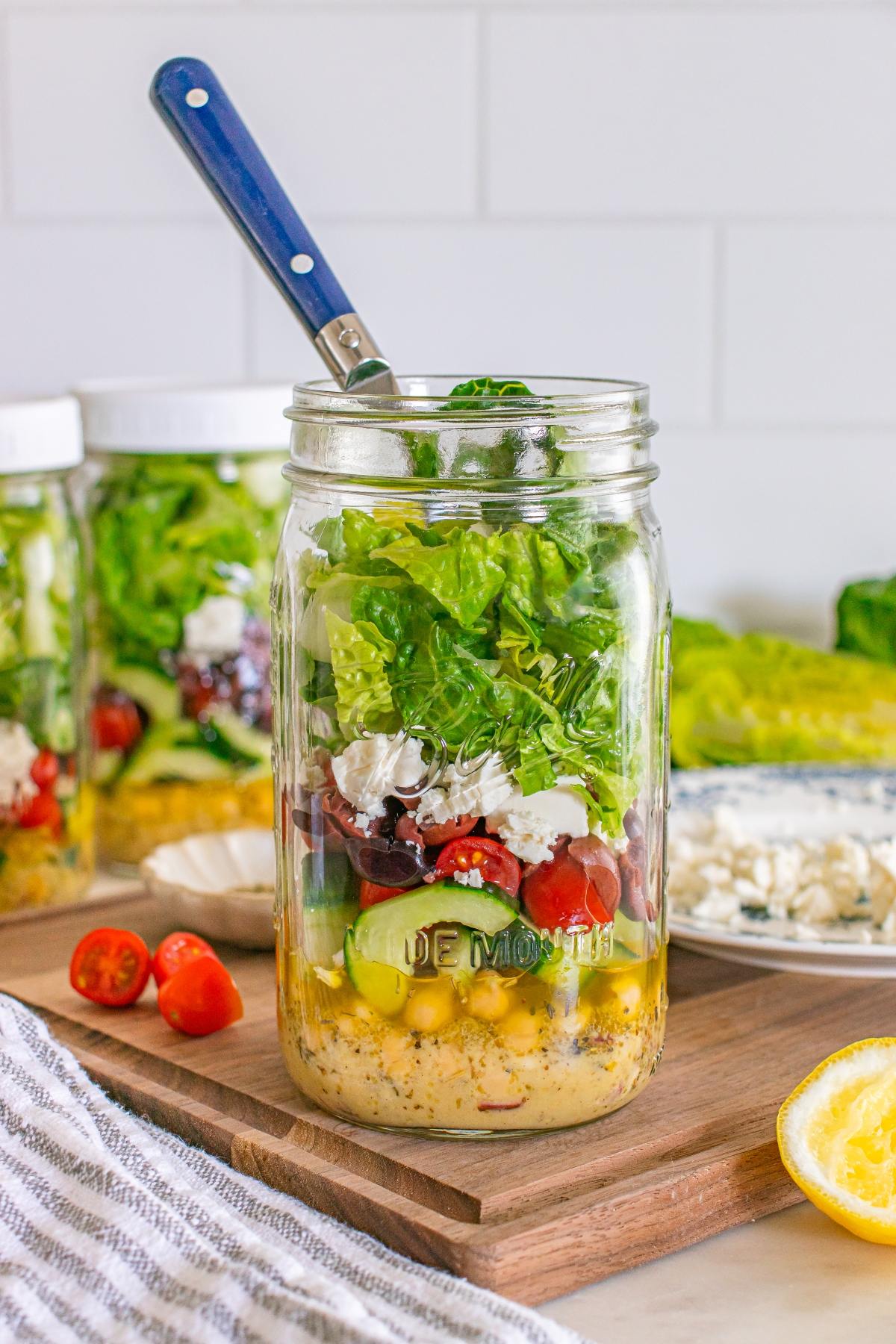 Mason jar salad with chickpeas, cherry tomatoes, cucumbers, lettuce, and feta cheese, with a fork inside.