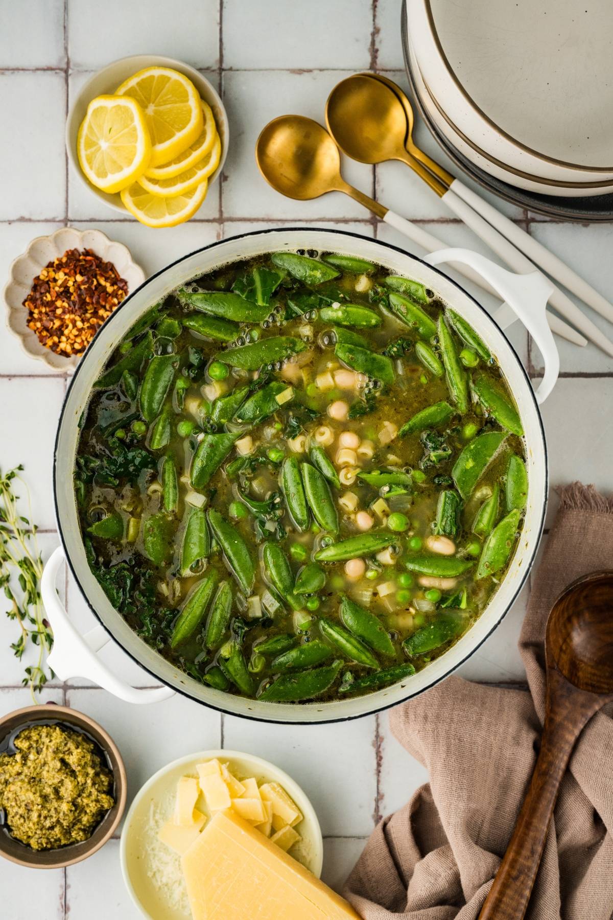 A pot of vegetable soup with beans and greens, surrounded by lemon slices, cheese, and seasonings.
