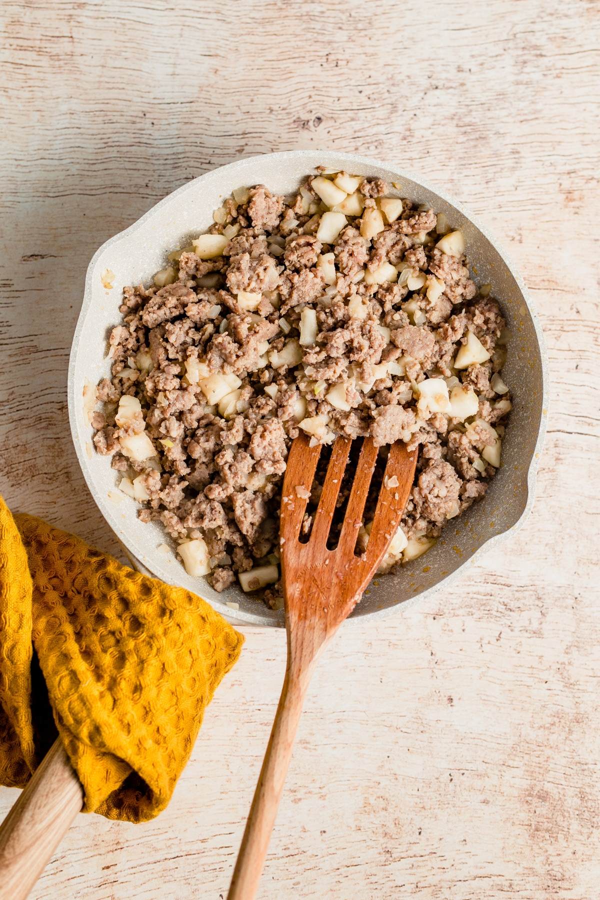 A skillet with cooked ground meat and diced vegetables, stirred with a wooden spatula, next to a yellow towel—perfect for an Easy family brunch recipe.