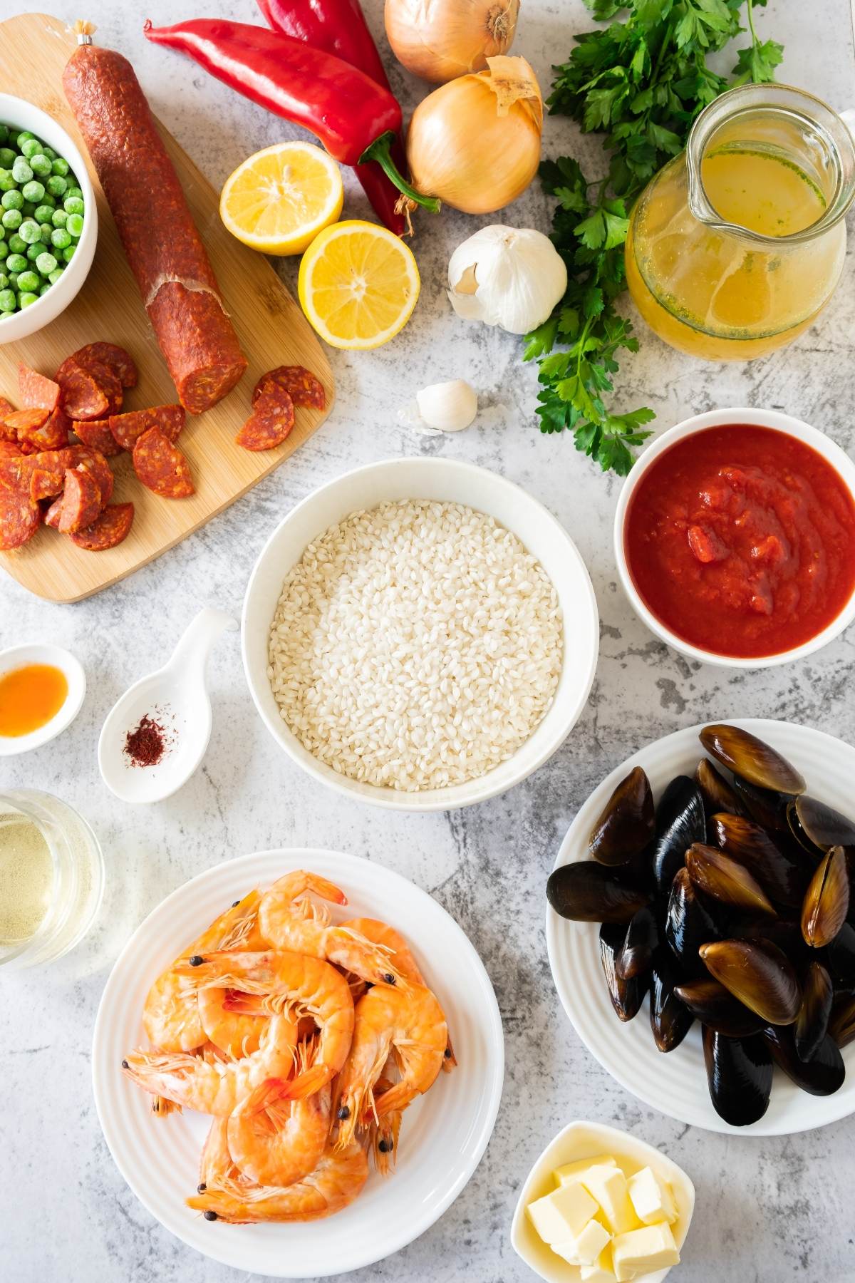 Flat lay of traditional Spanish paella ingredients: rice, shrimp, mussels, chorizo, peas, tomatoes, broth, onions, peppers, and seasonings—perfect for creating delicious seafood and chorizo paella at home.