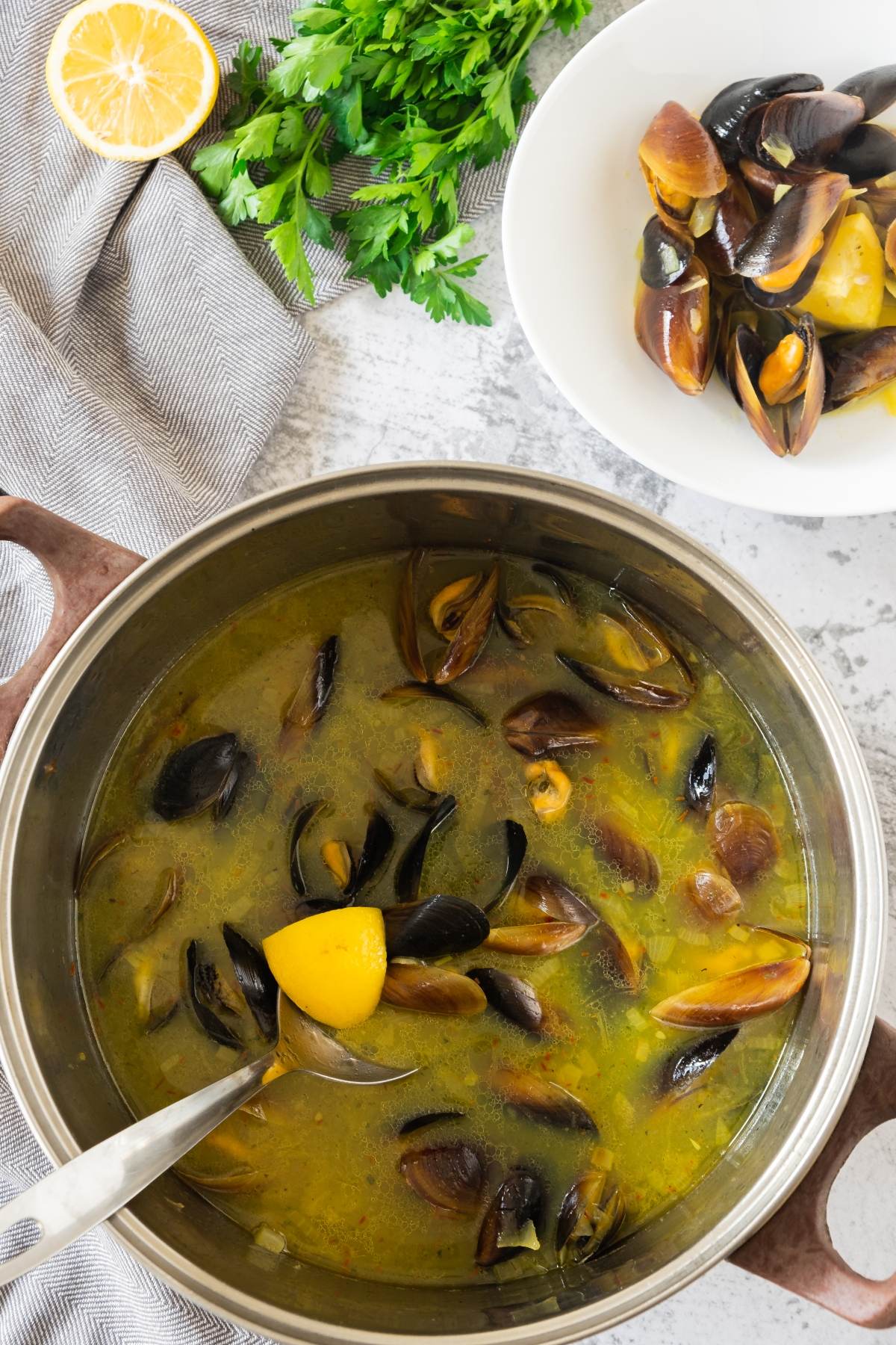 A pot of mussels in broth with lemon, alongside a bowl of empty shells and fresh parsley—a perfect starter before enjoying an easy seafood paella recipe.
