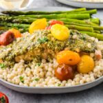 Plate with couscous, roasted asparagus, cherry tomatoes, and pesto-topped chicken—perfect for fans of easy sheet pan salmon and asparagus dinners.