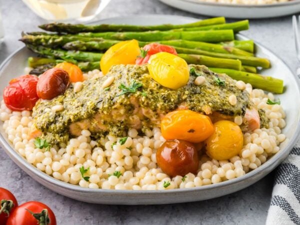 Plate with couscous, roasted asparagus, cherry tomatoes, and pesto-topped chicken—perfect for fans of easy sheet pan salmon and asparagus dinners.