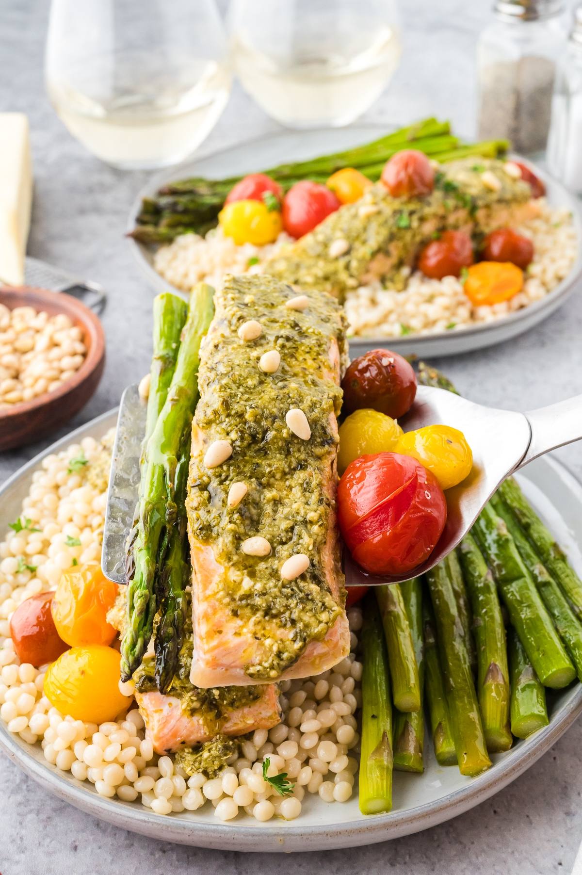 A plate with pesto salmon, asparagus, cherry tomatoes, and couscous, served with pine nuts on top.