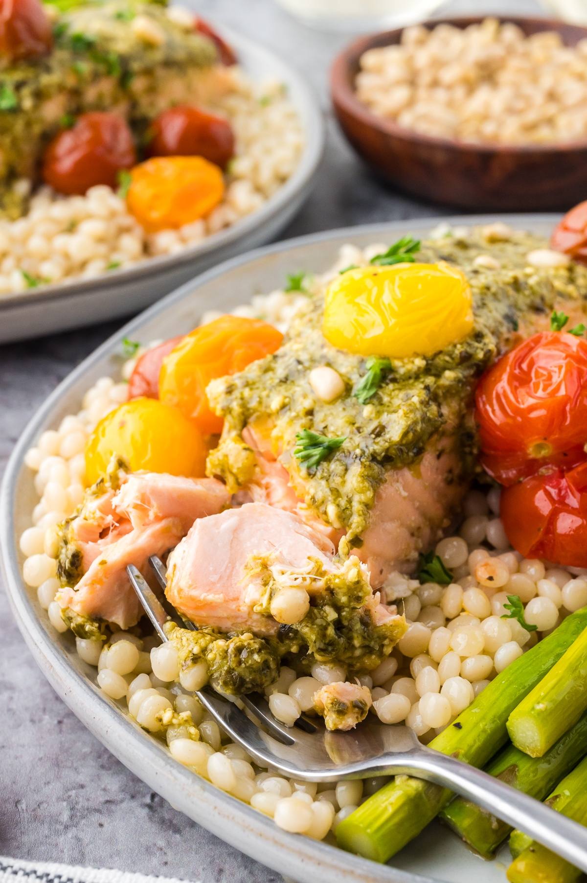 A plate of couscous with salmon, pesto sauce, cherry tomatoes, and asparagus, with a forkful of salmon.