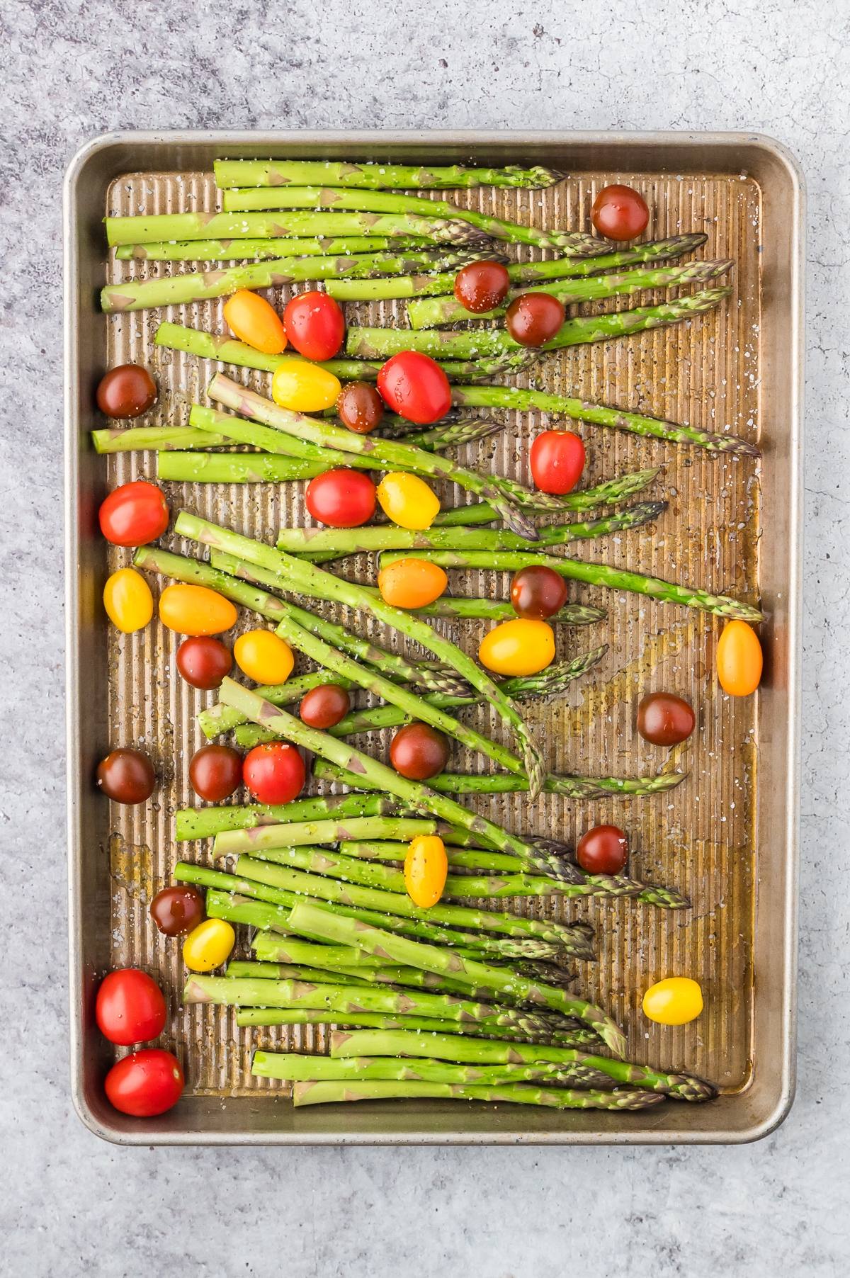 Asparagus and cherry tomatoes on a baking sheet, ready for roasting.