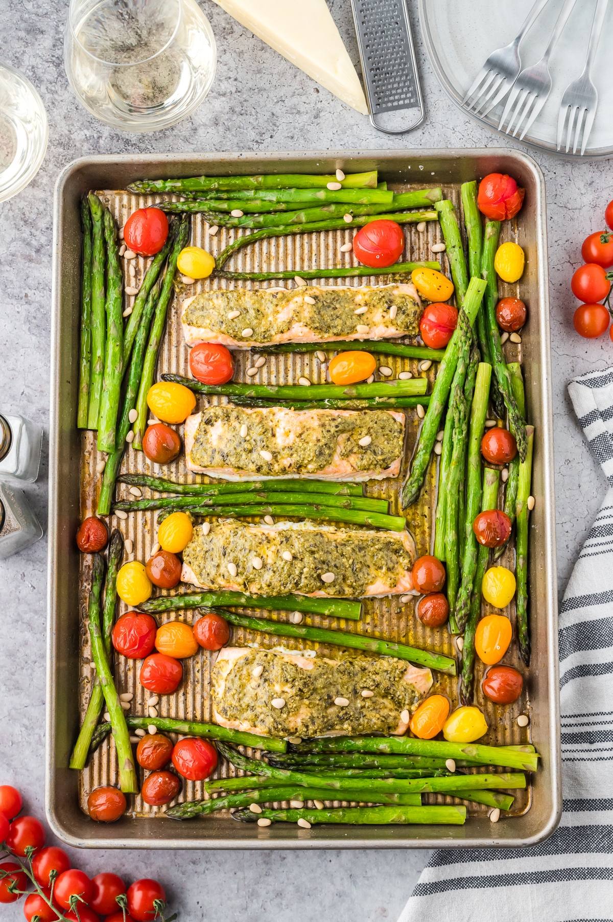 Sheet pan with four pesto-topped salmon fillets, asparagus, and cherry tomatoes, ready to serve.