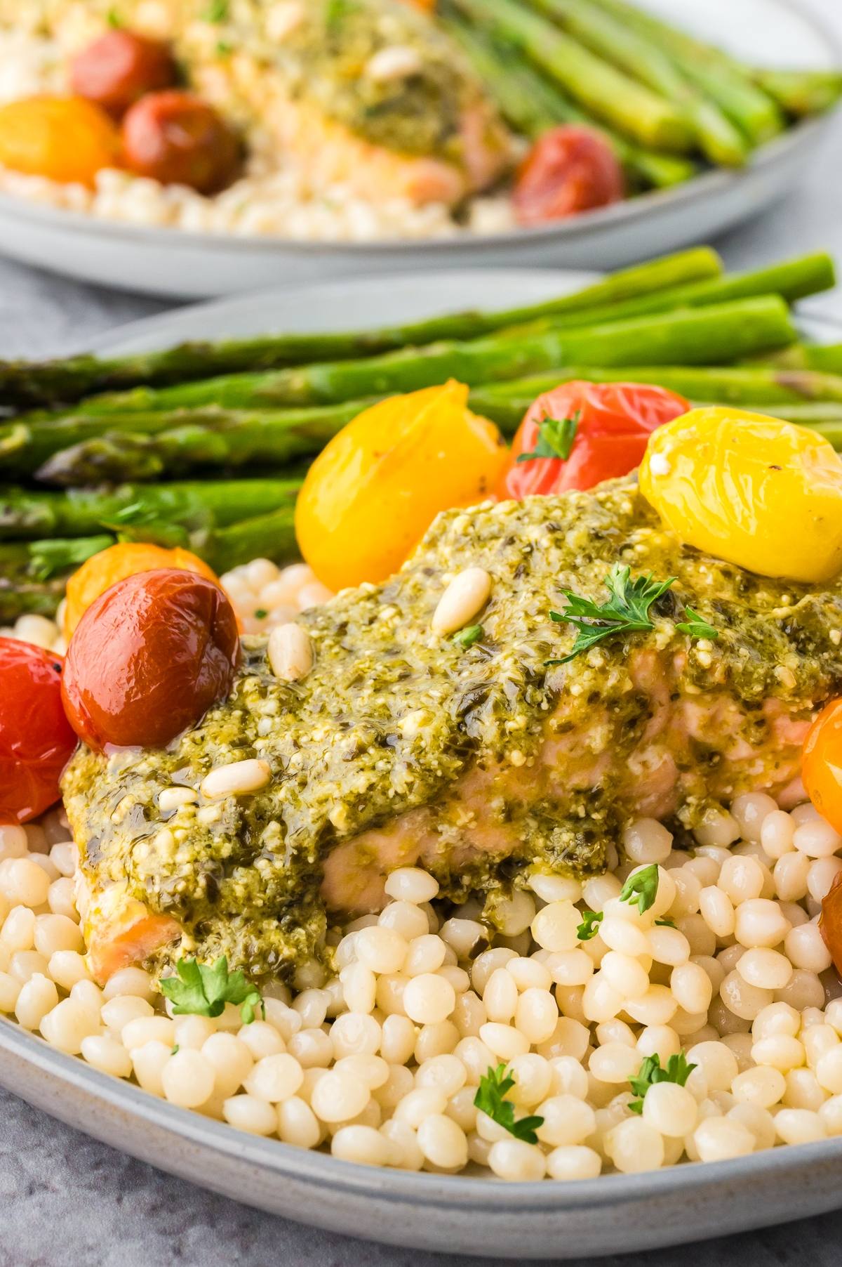 Salmon with pesto, couscous, roasted tomatoes, and asparagus on a plate.