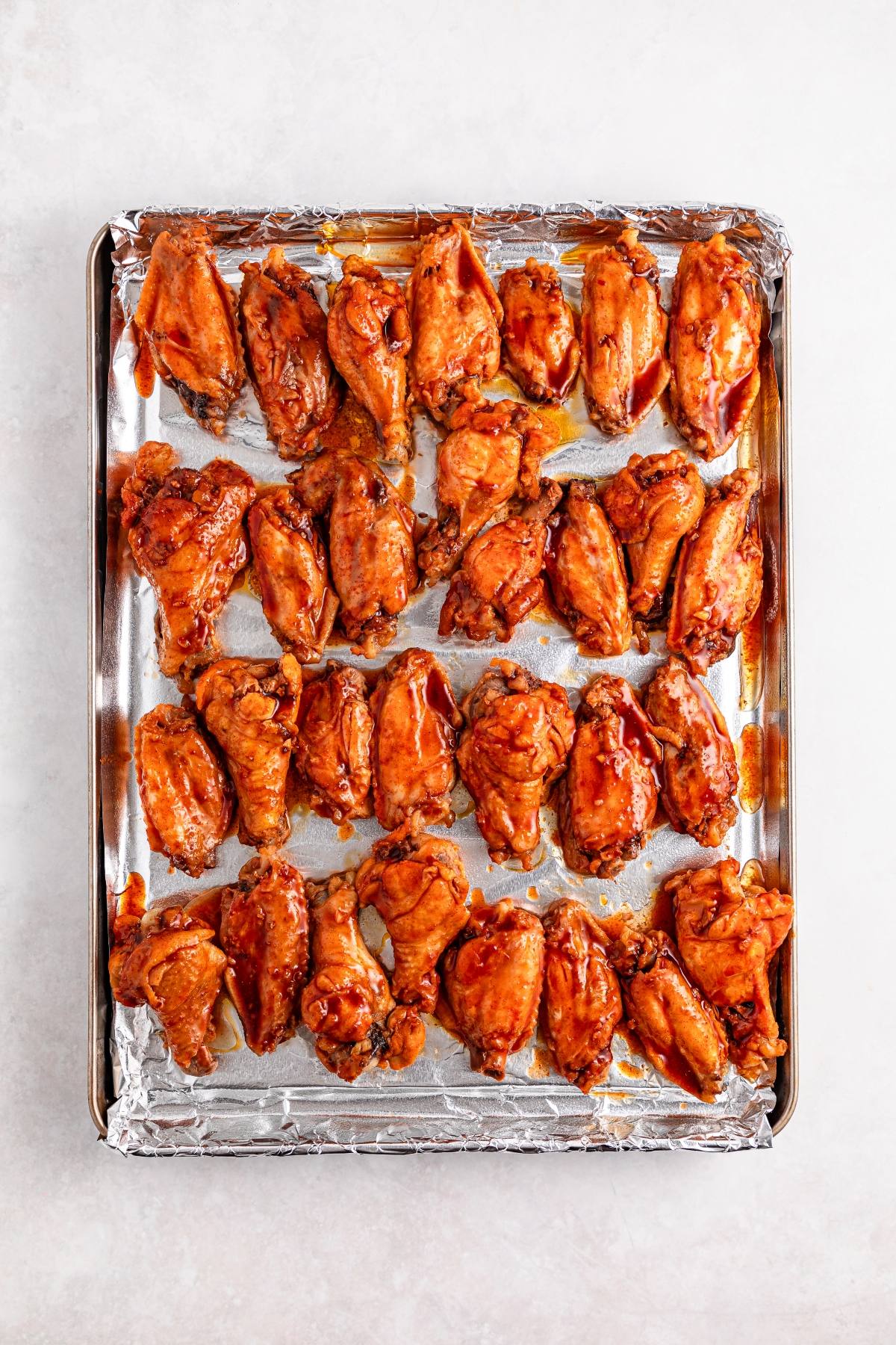 Baked chicken wings coated in sauce arranged on a foil-lined baking sheet.