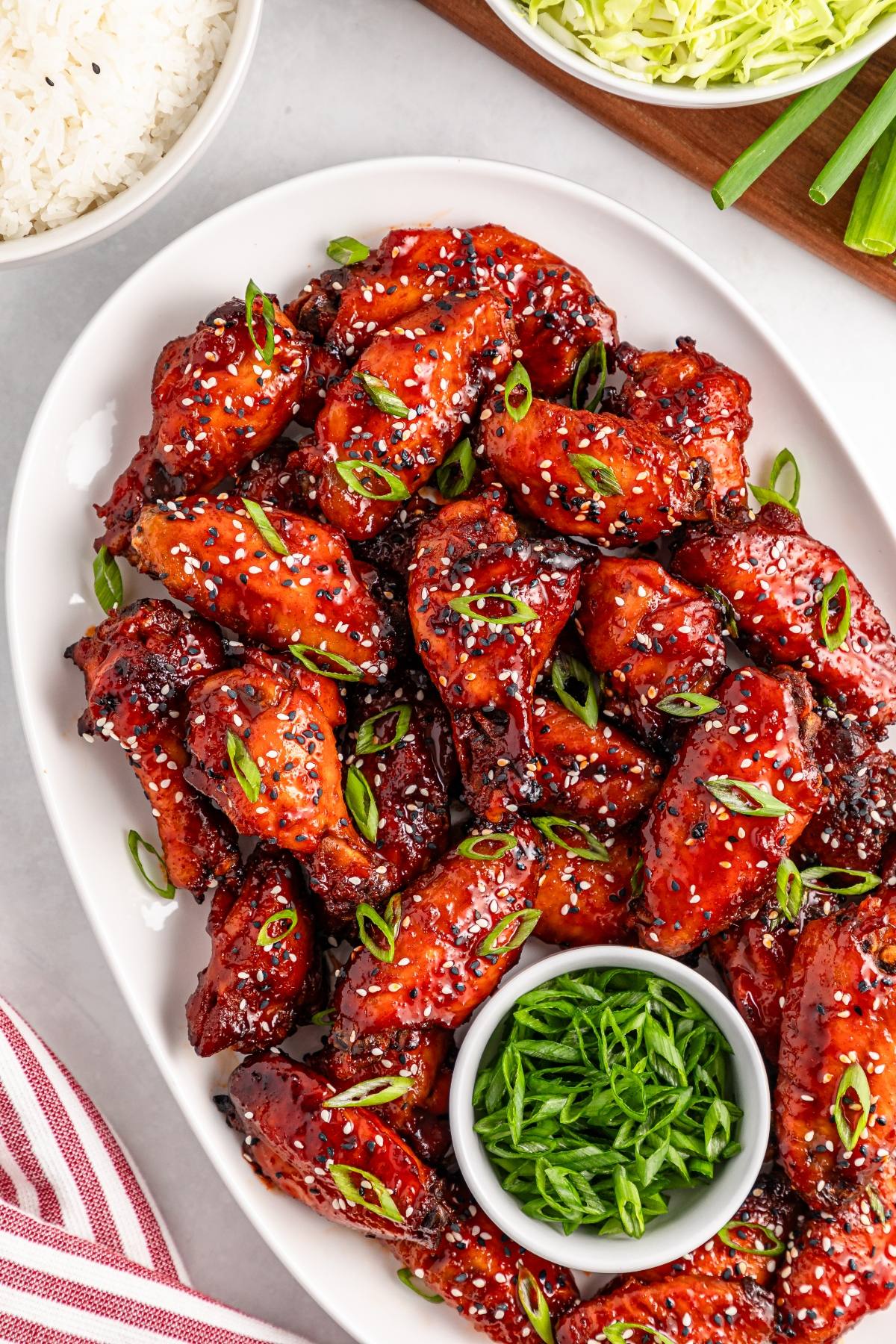 Plate of glazed chicken wings garnished with sesame seeds and green onions, with a bowl of sliced green onions.