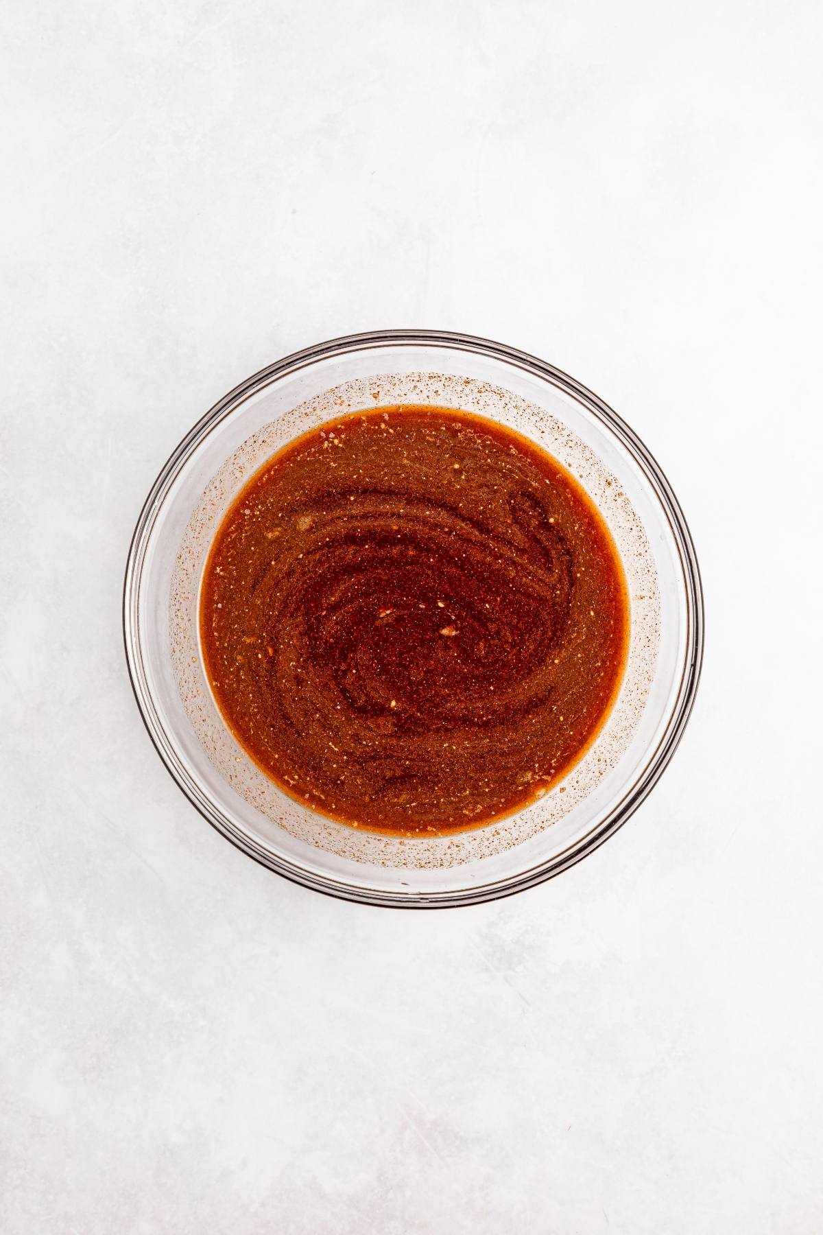 A glass bowl filled with a reddish-brown sauce, sitting on a white surface.