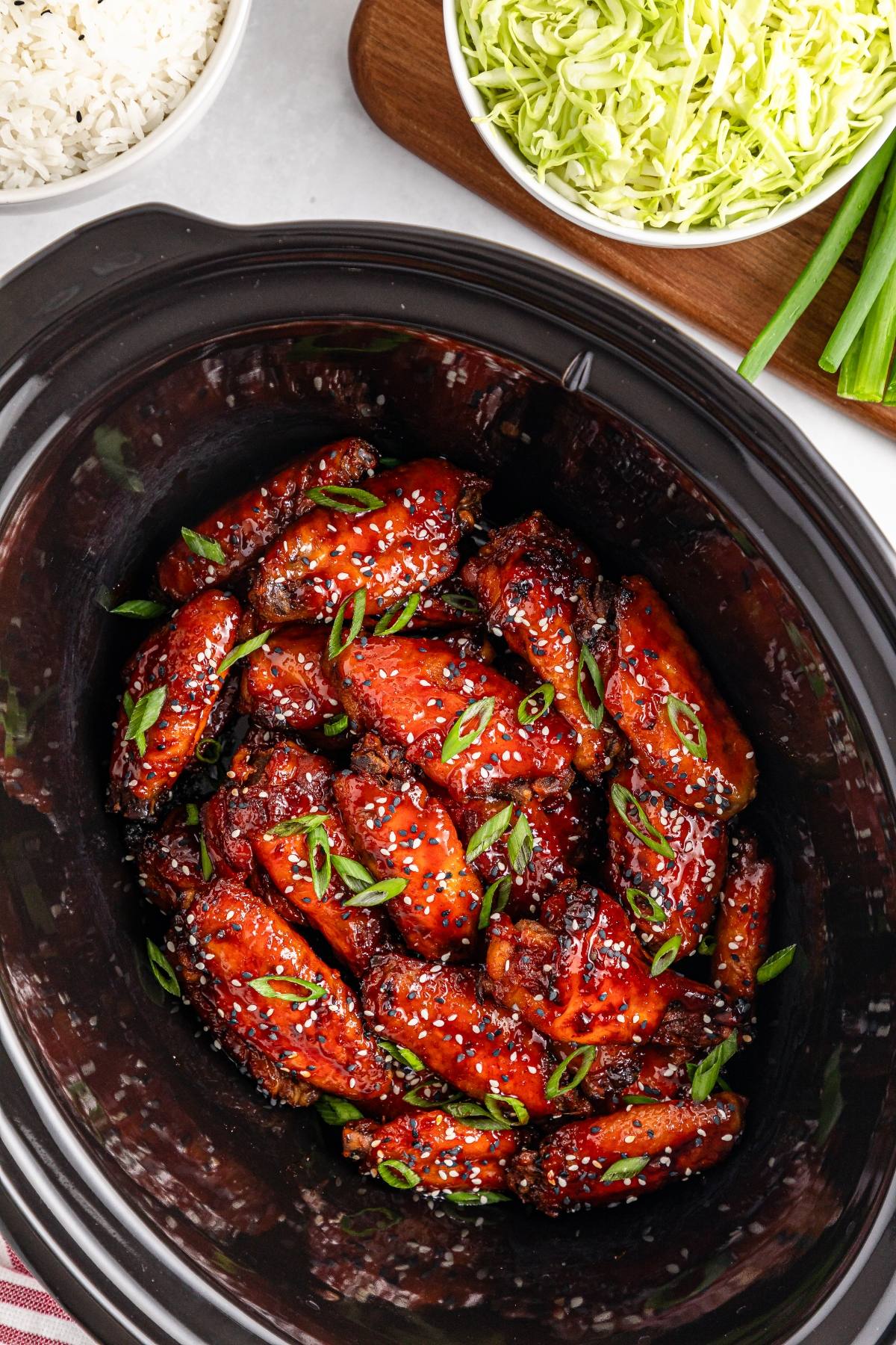 Chicken wings with sesame seeds and chopped green onions in a slow cooker, with cabbage and rice on the side.