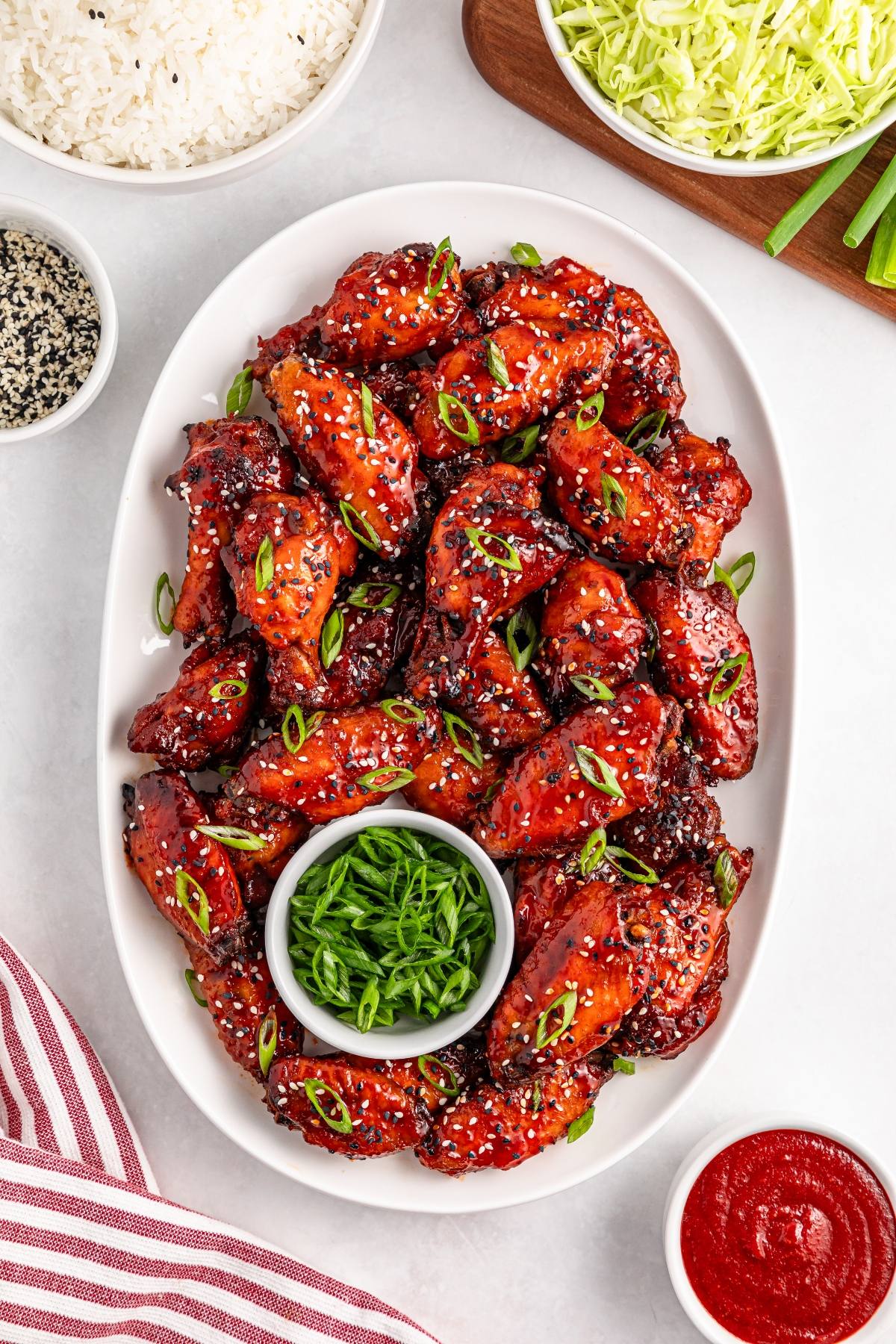 A platter of sticky glazed chicken wings garnished with sesame seeds and green onions, surrounded by sides.