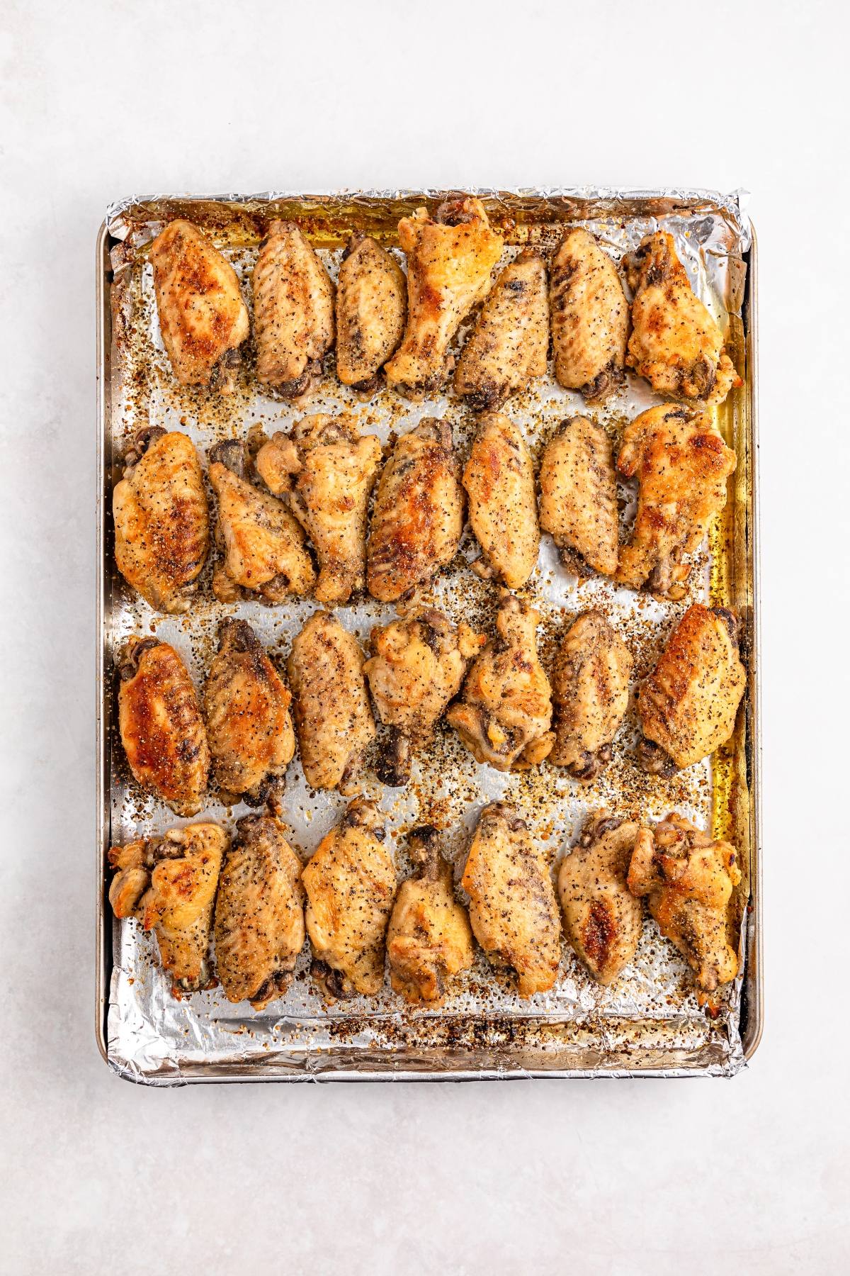 Baked chicken wings on a foil-lined baking sheet, seasoned and arranged in rows.