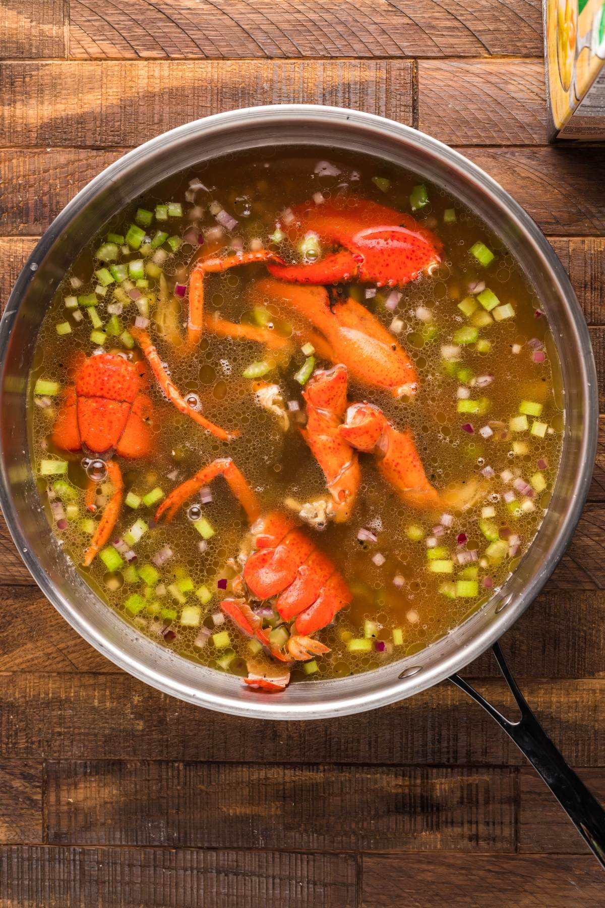 A pot of broth with lobster shells, chopped celery, onions, and carrots on a wooden surface—perfect ingredients for starting a rich and creamy seafood soup or preparing a flavorful Crockpot seafood bisque.