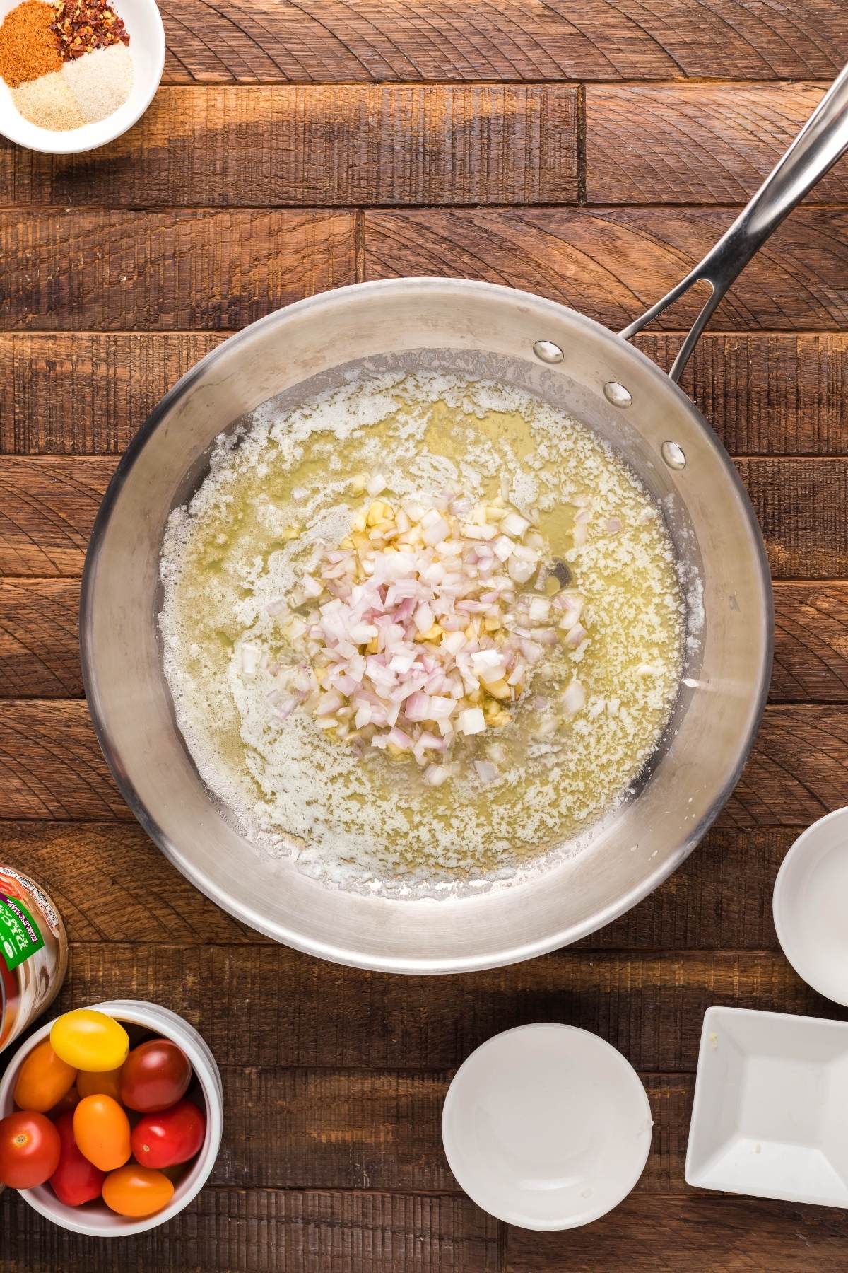 A pan with melted butter, chopped shallots, and garlic on a wooden surface—perfect for starting a rich Slow Cooker Seafood Bisque—surrounded by bowls ready to serve.