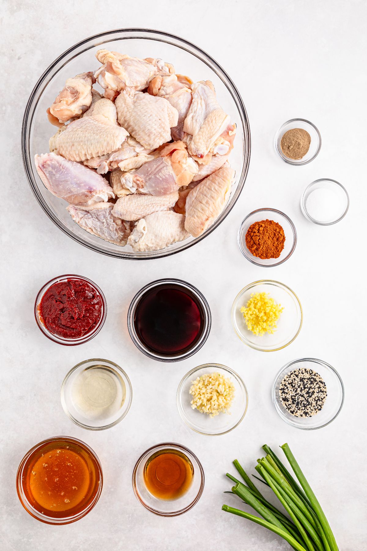 Raw chicken wings in a bowl surrounded by spices, sauces, chopped garlic, ginger, and fresh green onions—perfect for making slow cooker spicy Korean wings.