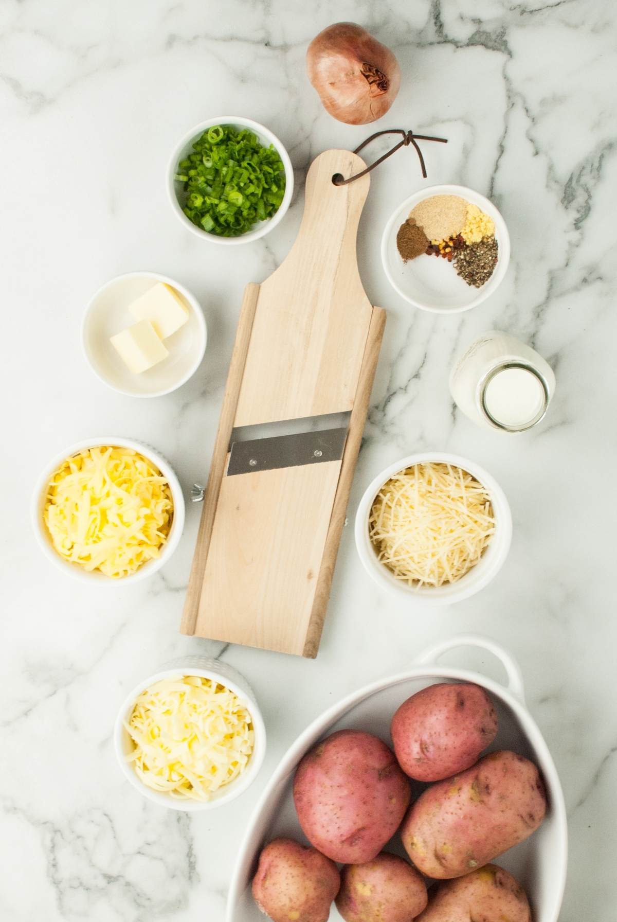 Ingredients for Smoked Gouda Scalloped Potatoes shown on a marble surface with a mandoline slicer—potatoes, cheese, and seasonings ready for delicious scalloped potatoes from scratch.