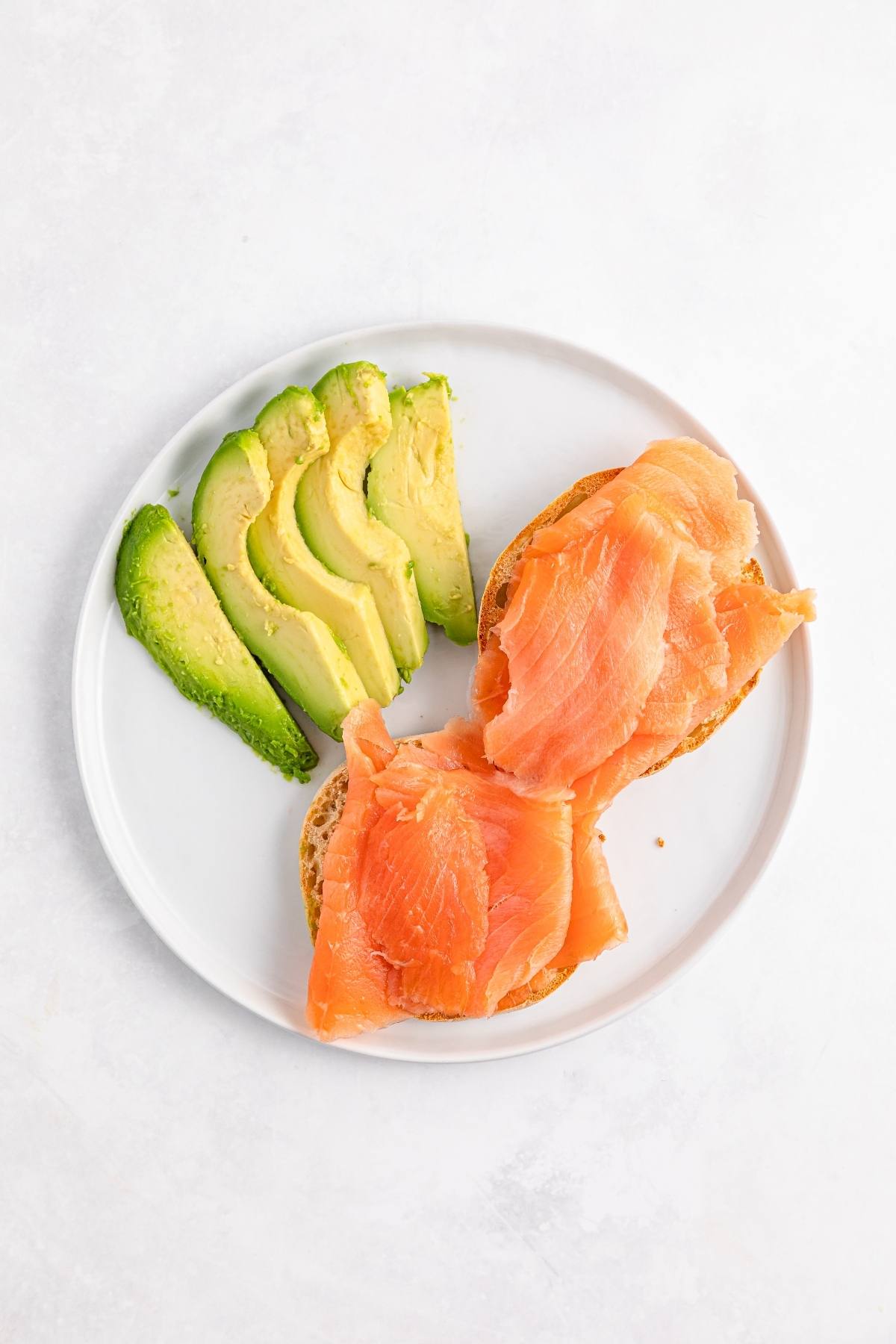 Sliced avocado and smoked salmon on toast arranged on a white plate.