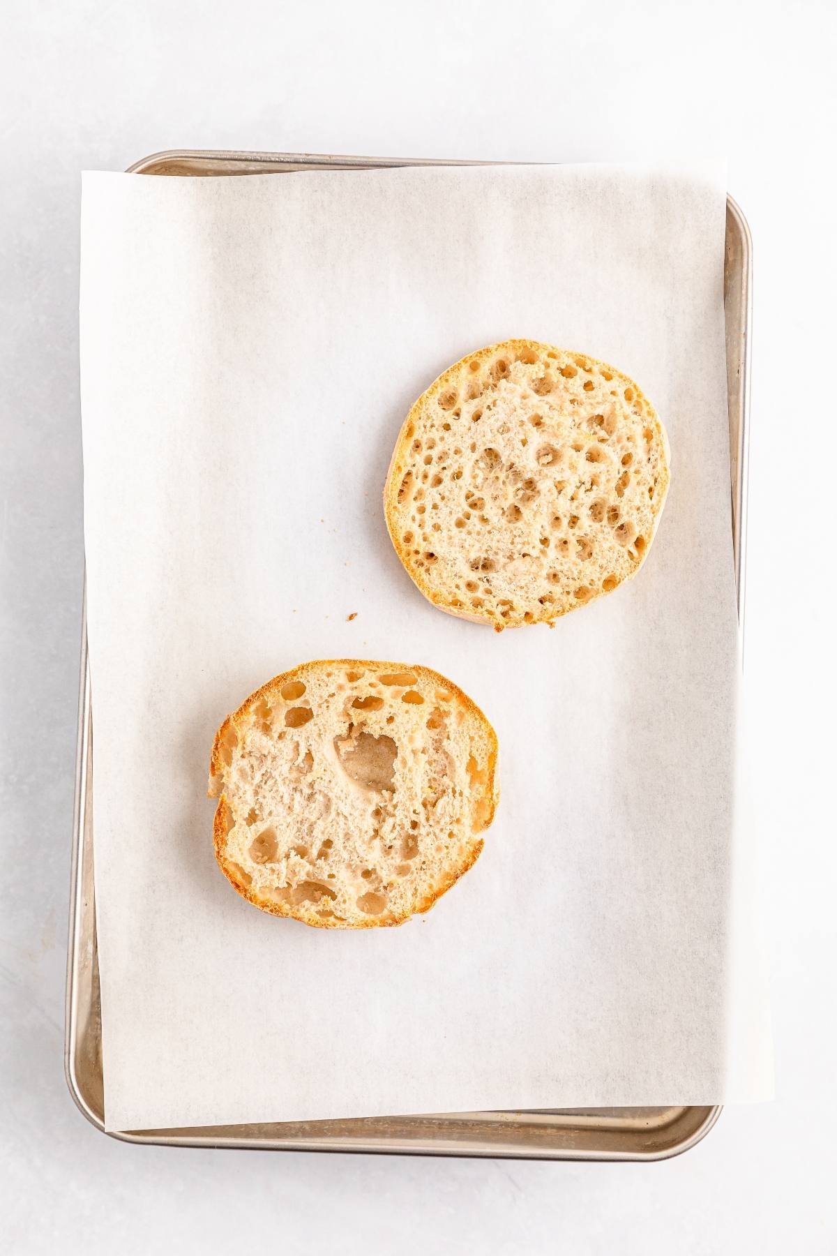 Two halves of an English muffin on parchment paper-lined baking sheet.