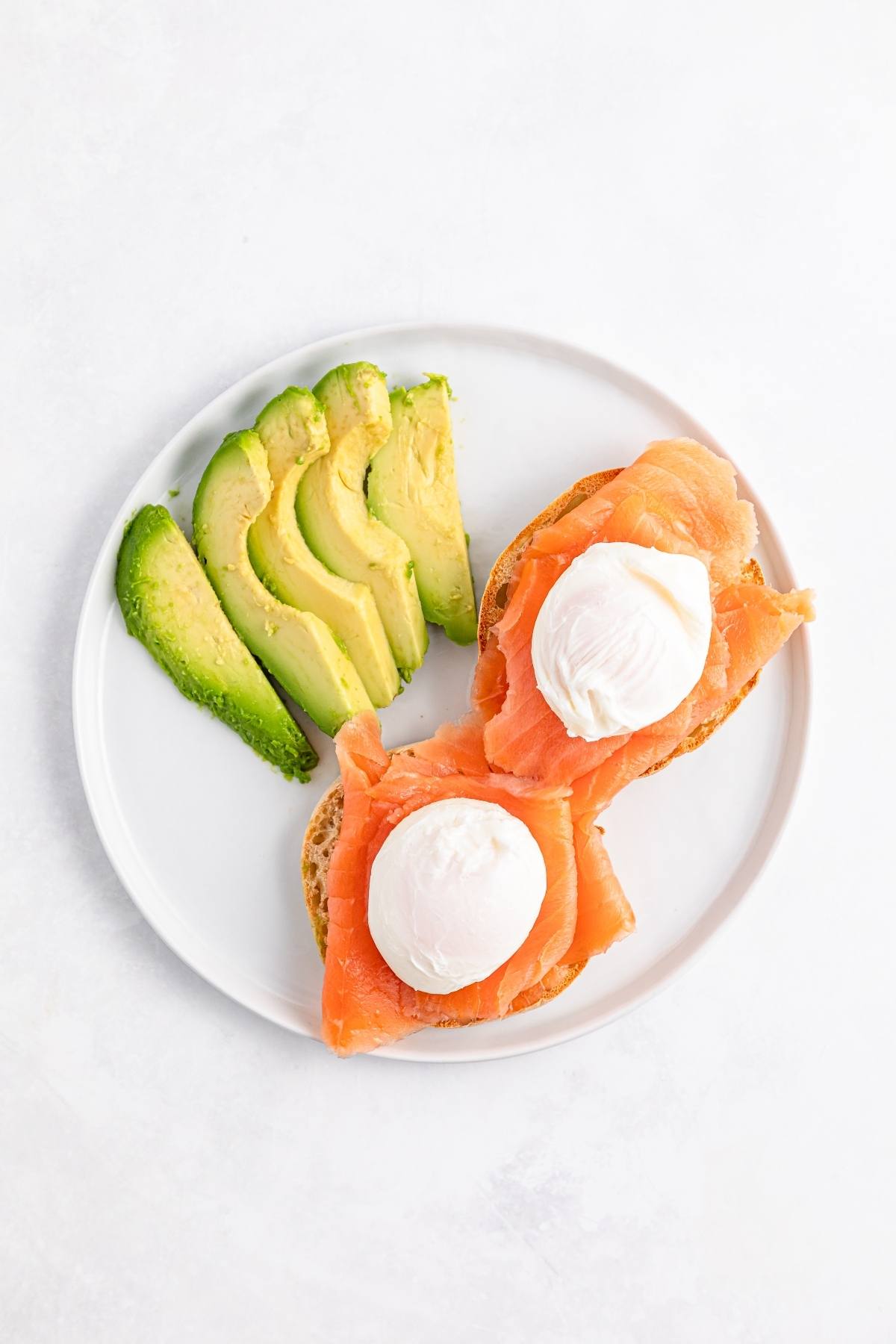 A plate with sliced avocado and two pieces of toast topped with smoked salmon and poached eggs.