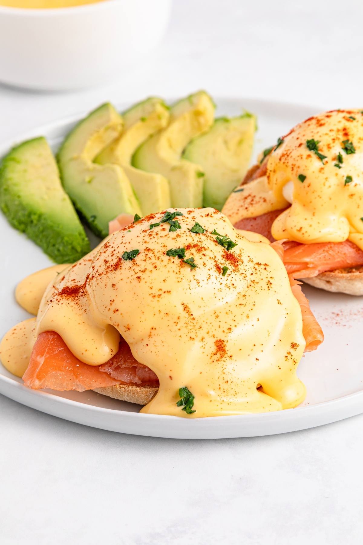 Eggs Benedict with smoked salmon and hollandaise sauce, served with sliced avocado on a white plate.