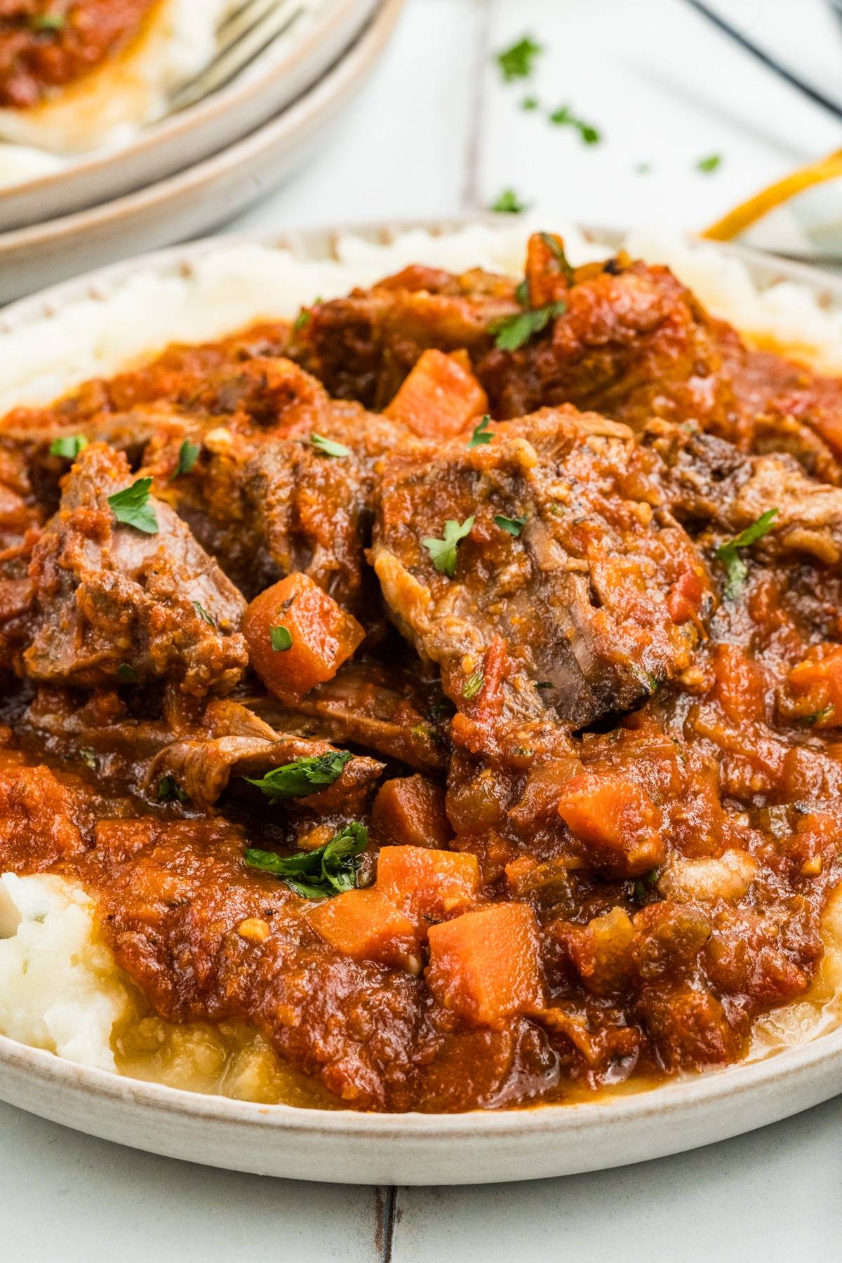 Beef stew with carrots and tomato sauce served over mashed potatoes on a white plate.