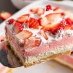 A close-up of a decadent strawberry lush dessert, featuring layers of whipped cream and fresh strawberry pieces on top.