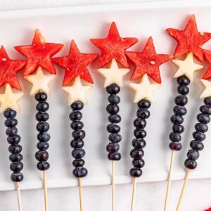 Watermelon Blueberry Sparklers Fruit skewers with blueberries, white melon stars, and watermelon stars arranged on a white rectangular plate.