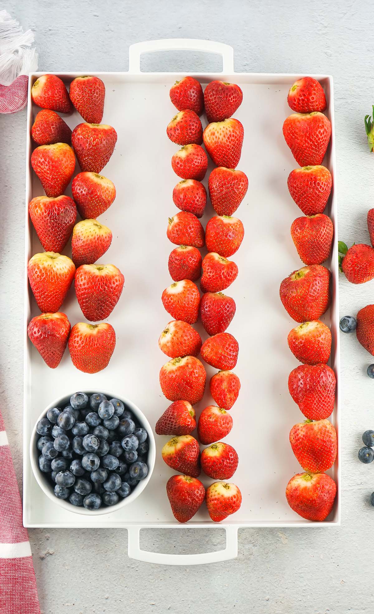 Tray with strawberries arranged in stripes and a bowl of blueberries in the corner, creating a festive Stars and Stripes Cheese Board reminiscent of the American flag.