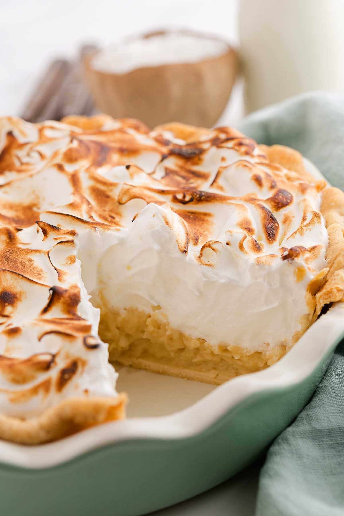 A creamy coconut meringue pie with a slice missing, showing off the fluffy topping and golden crust.