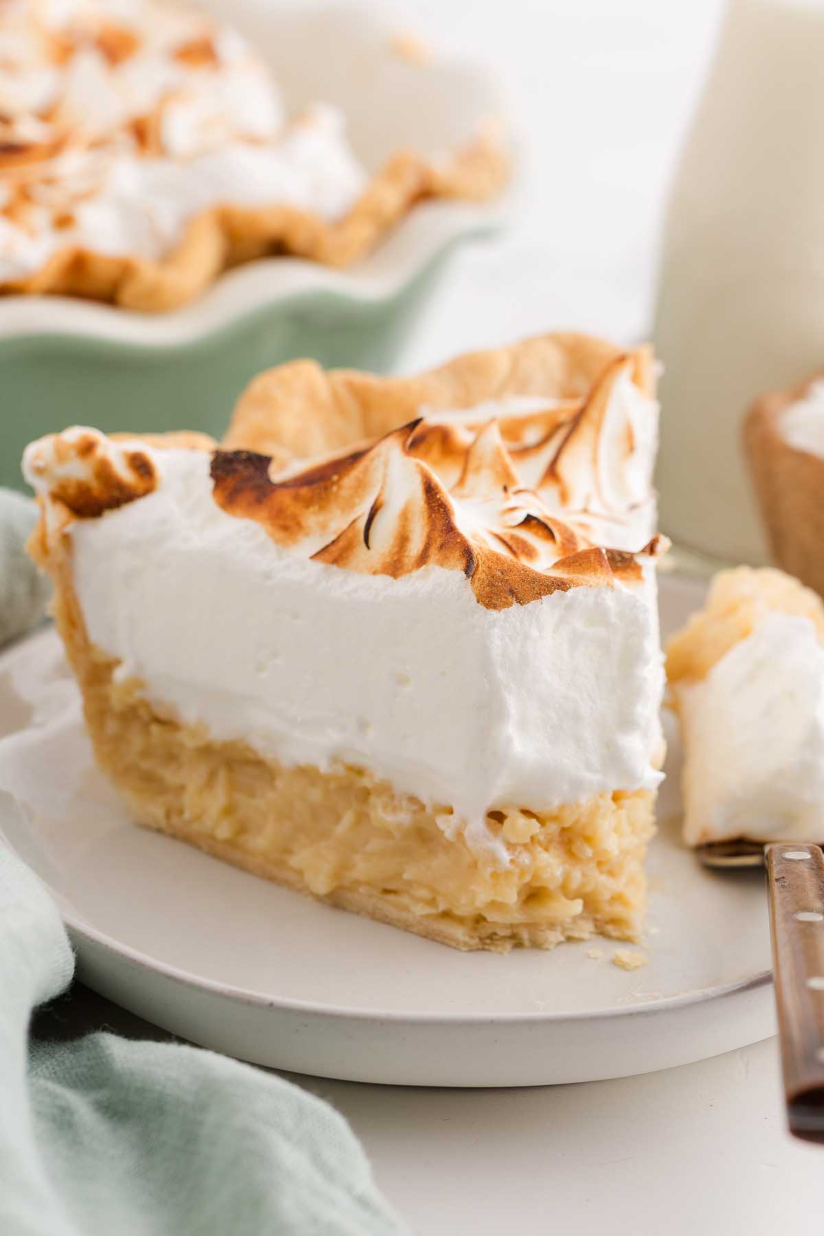 A slice of coconut meringue pie with toasted meringue topping sits on a white plate.