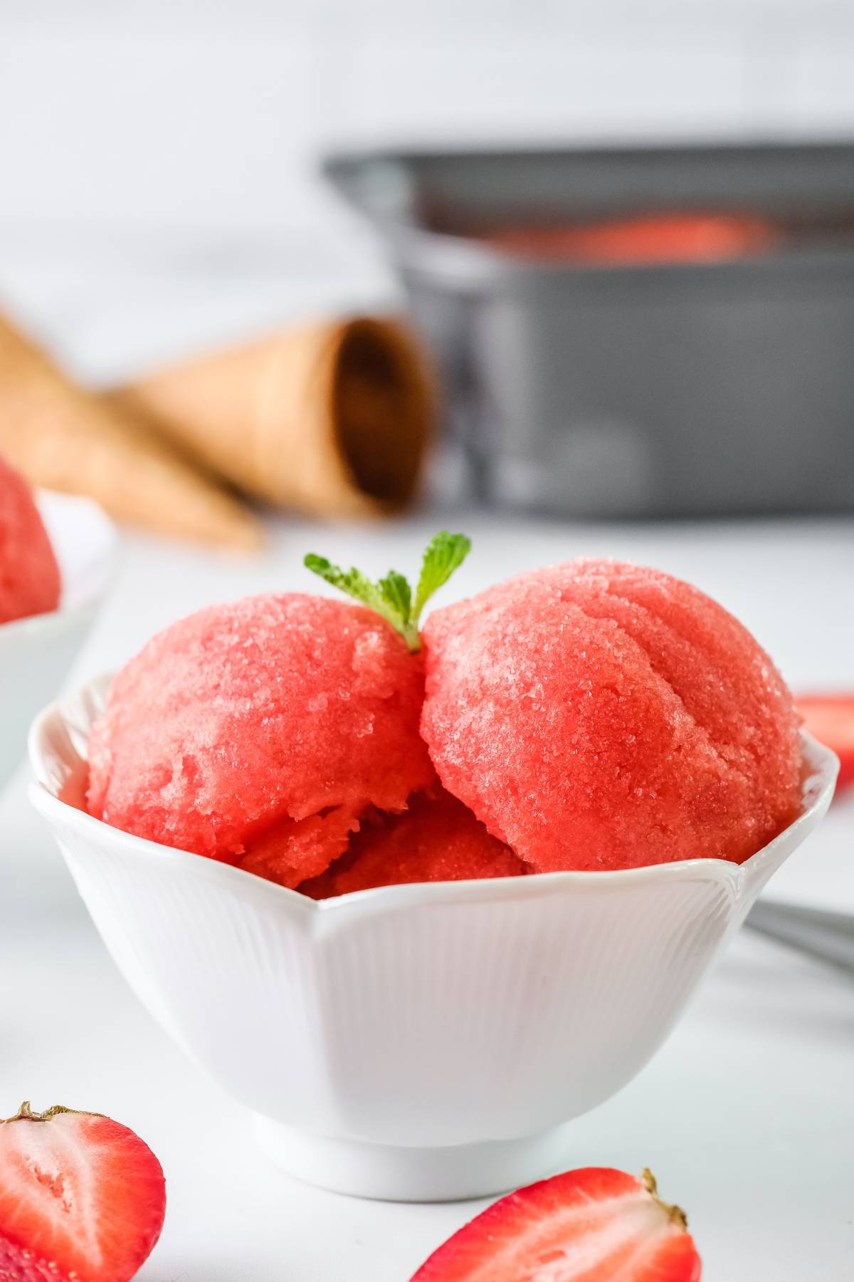 Refreshing Strawberry Sorbet: Two scoops of quick and easy sorbet made with frozen strawberries, served in a white bowl, garnished with a mint sprig and fresh strawberries on the side.