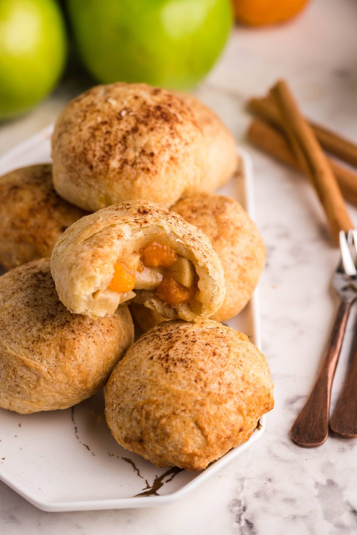 Golden baked air fryer dumplings with cinnamon on a white plate, one broken open to reveal the apple filling—an irresistible autumn air fryer dessert.