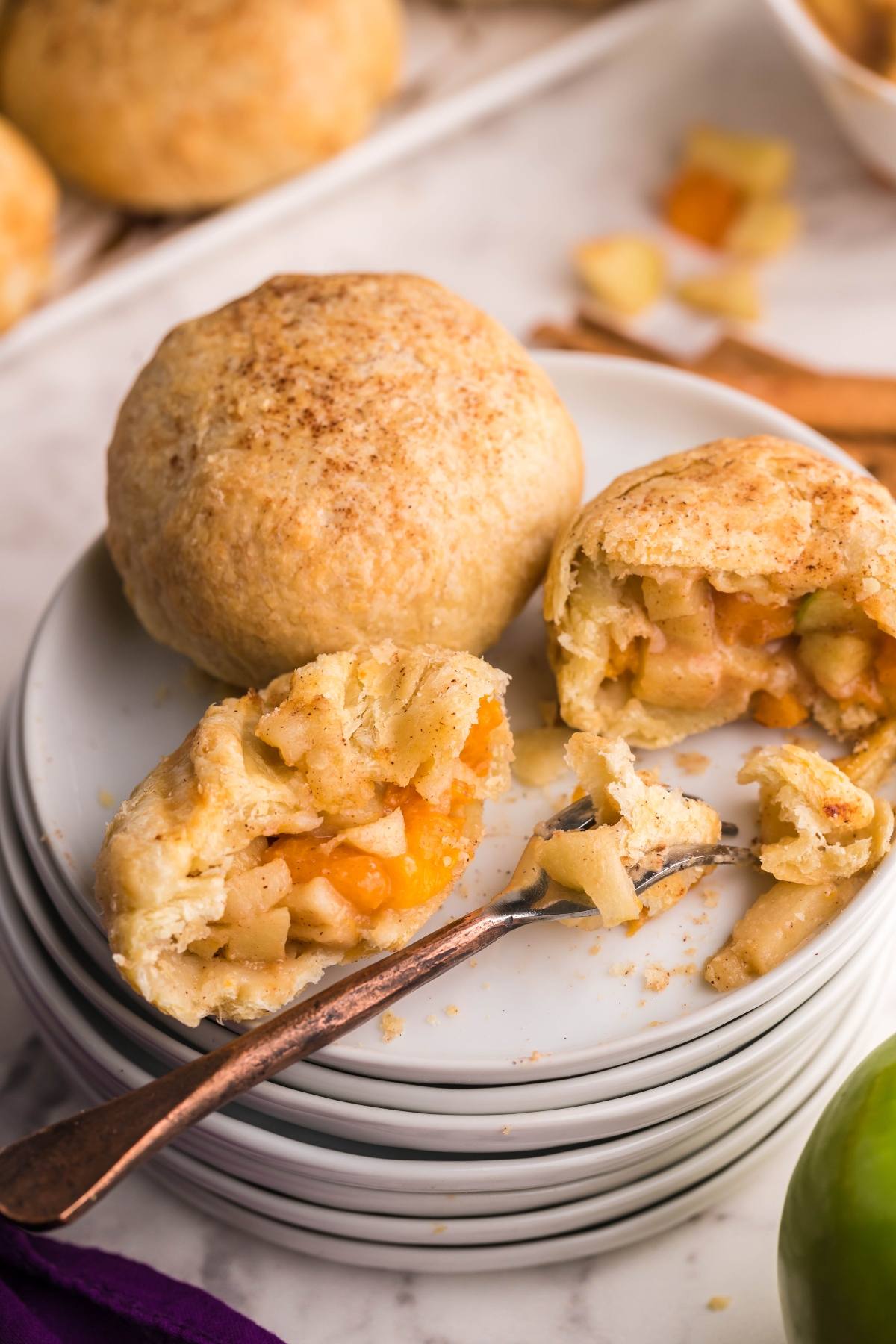 Two baked Air Fryer Apricot Apple Dumplings, one whole and one cut open to reveal spiced apple filling, are stacked on white plates—an irresistible Autumn air fryer dessert.