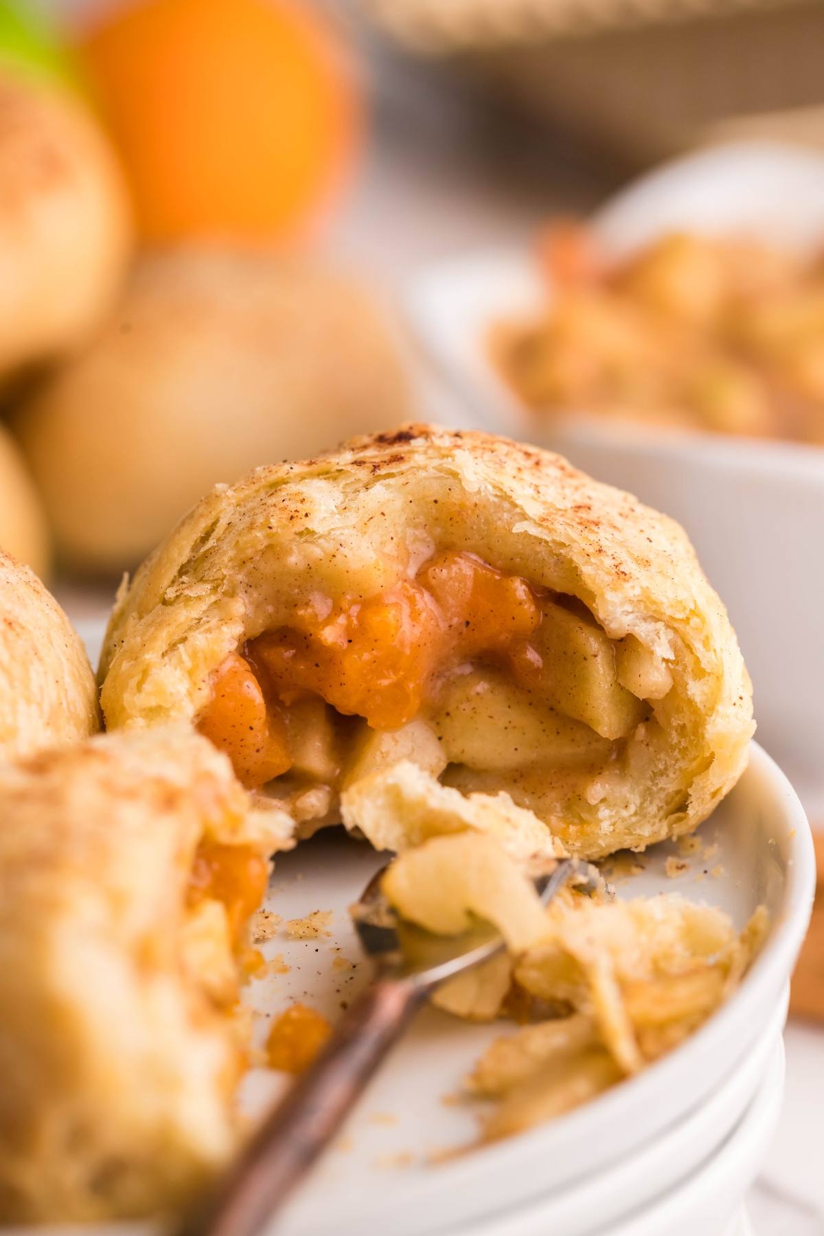 A baked pastry filled with apple pie filling, broken open on a plate with a fork—just like delicious air fryer dumplings or Air Fryer Apricot Apple Dumplings made quickly and easily at home.