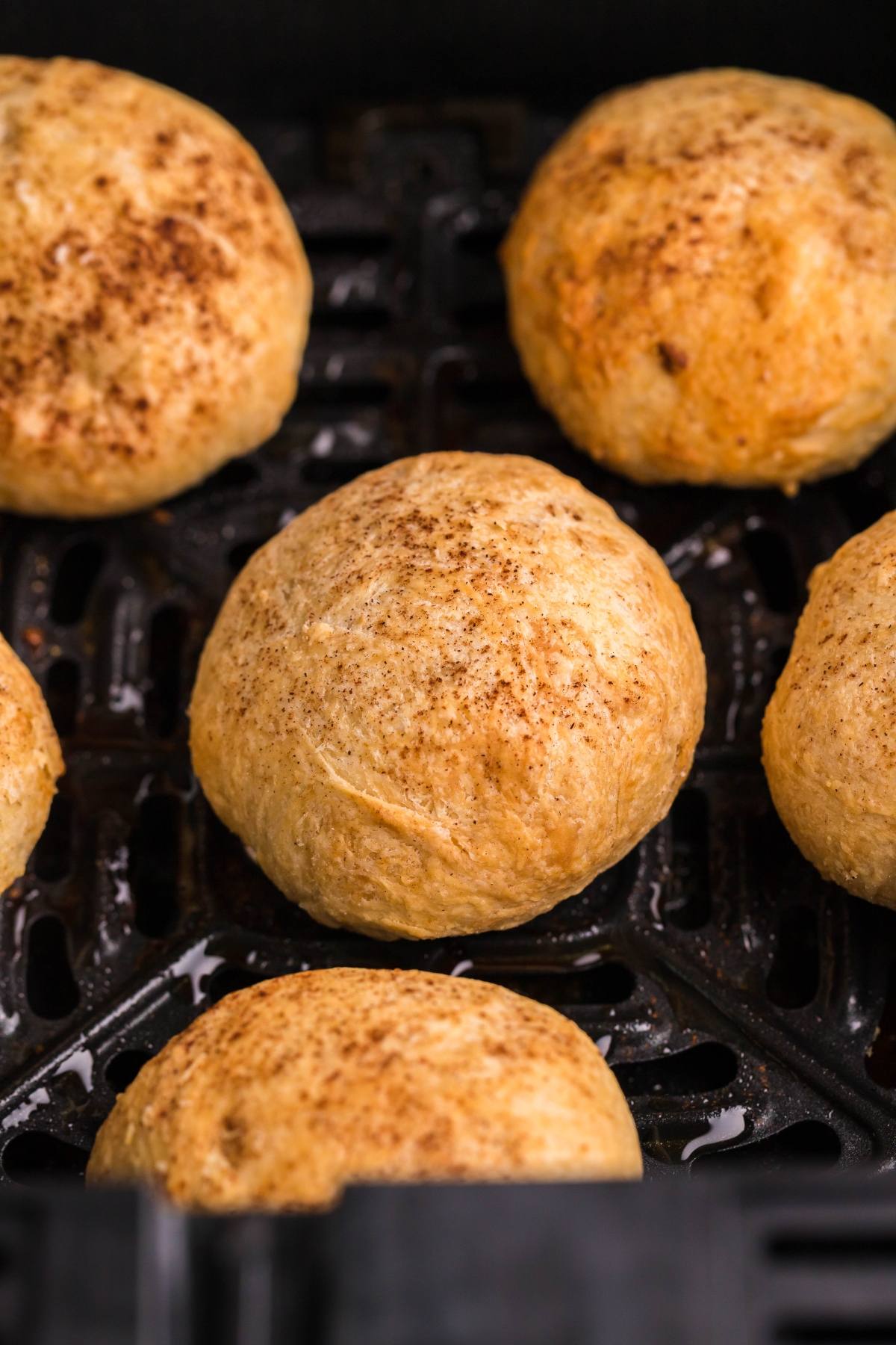 Six golden brown puff pastry dumplings bake in an air fryer basket, sprinkled lightly with cinnamon—a cozy autumn air fryer dessert.