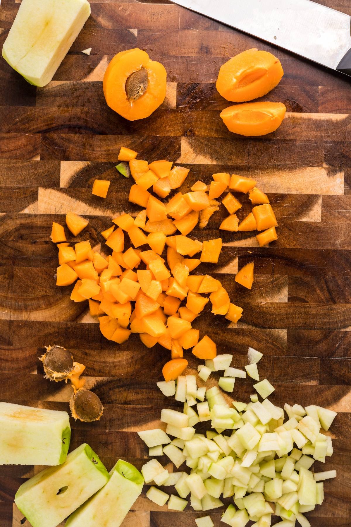 Diced apples and apricots on a wooden cutting board, ready to become delicious puff pastry dumplings—an easy Autumn air fryer dessert with fruit pieces and a knife nearby.