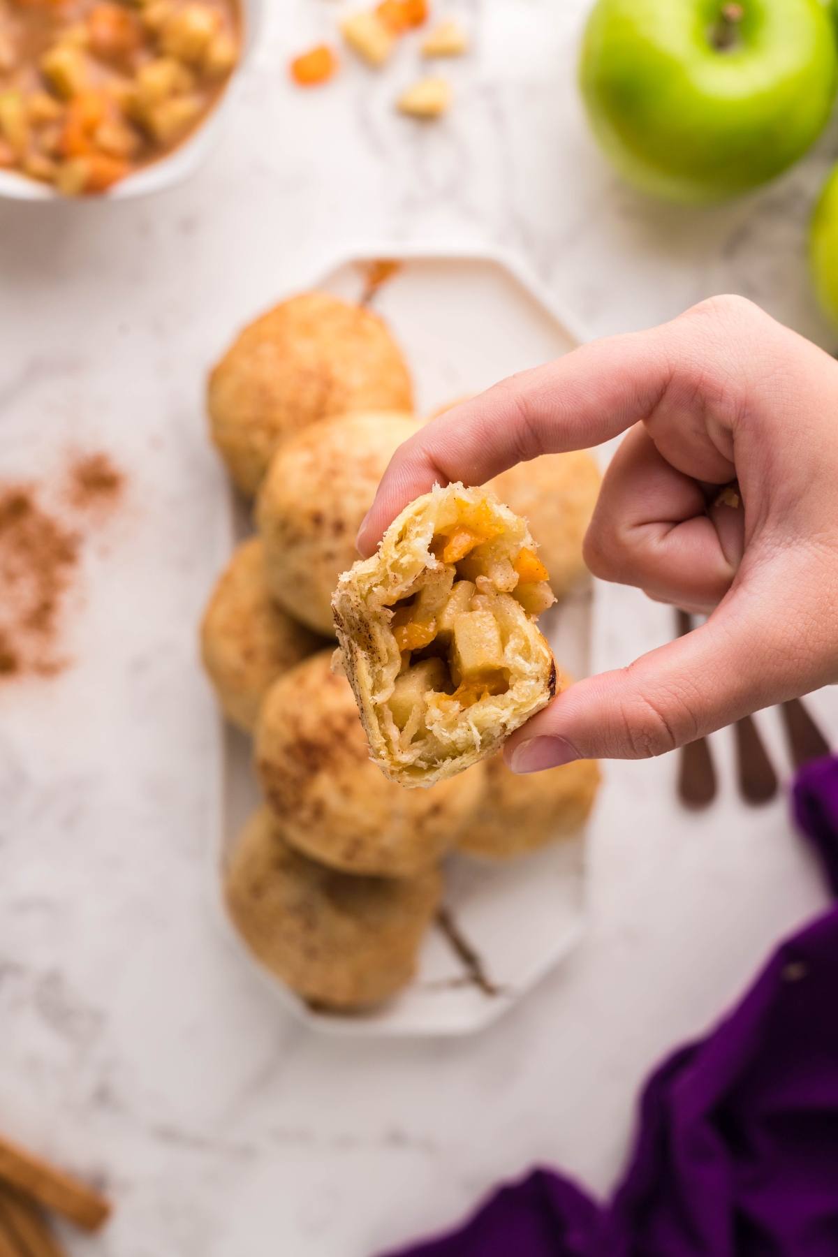 A hand holding a baked Air Fryer Apricot Apple Dumpling filled with apple chunks, with more air fryer dumplings on a plate below—perfect as an autumn air fryer dessert.