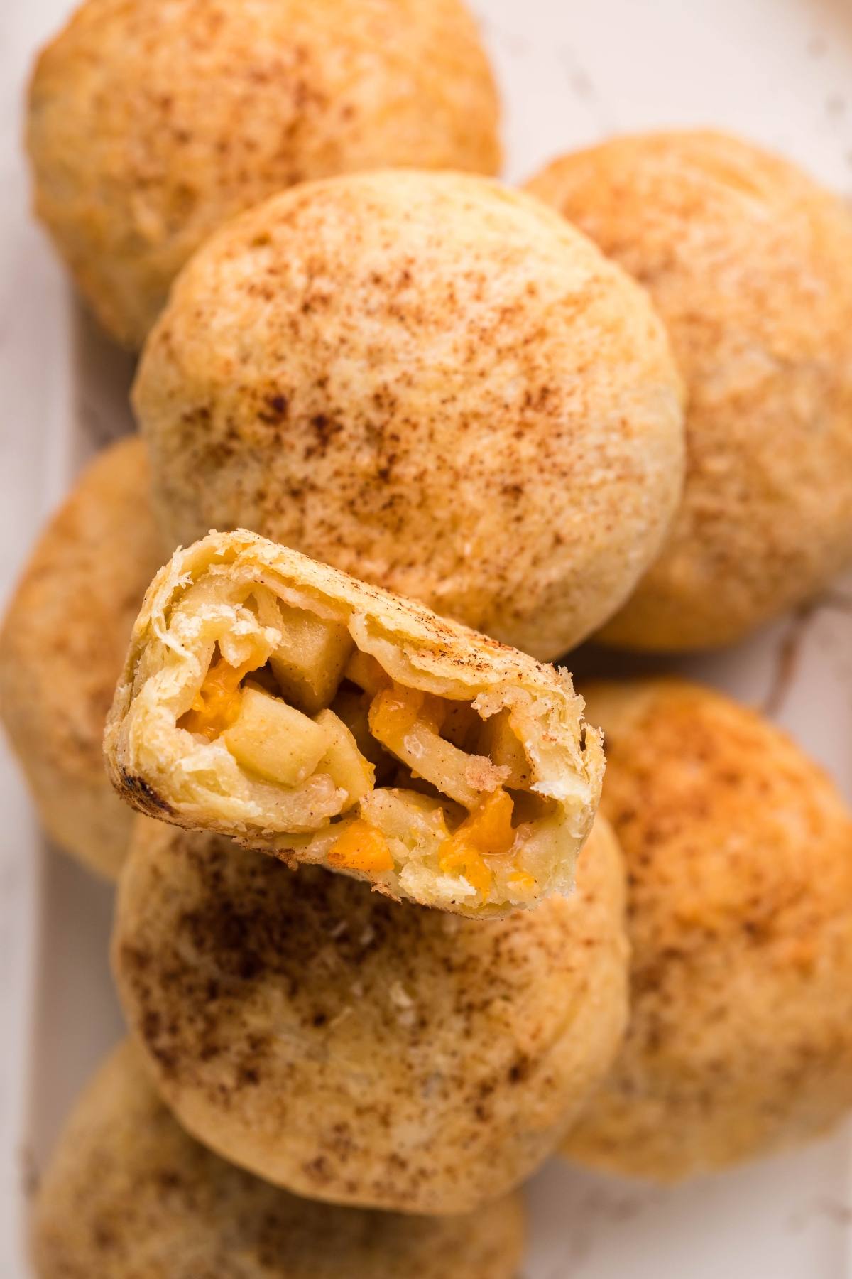 Close-up of round puff pastry dumplings, one cut open to reveal a spiced apple filling, dusted with cinnamon—an irresistible Autumn air fryer dessert.